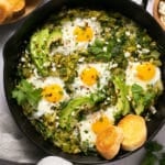 cast iron skillet with eggs, green sauce, avocado, and biscuits