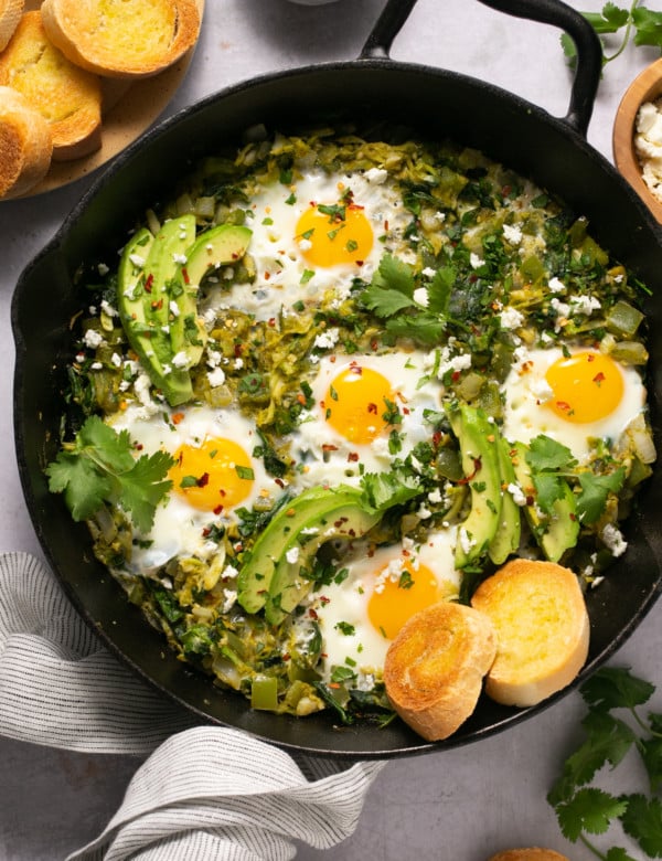 cast iron skillet with eggs, green sauce, avocado, and biscuits