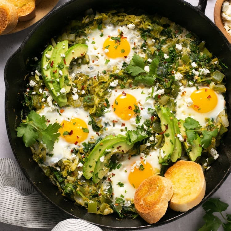 cast iron skillet with eggs, green sauce, avocado, and biscuits