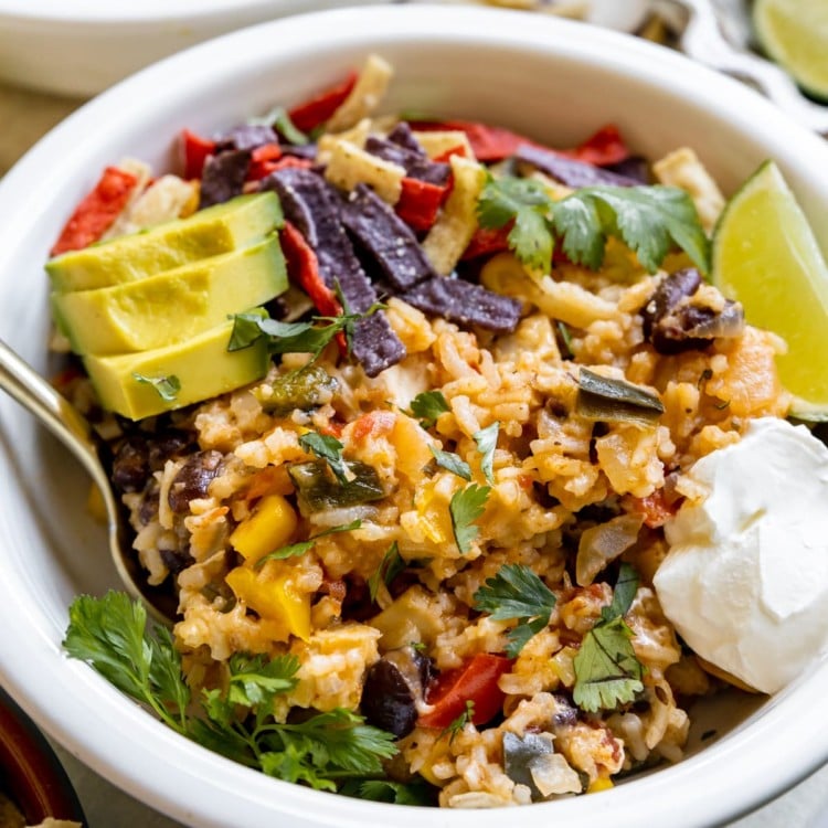white bowl with rice mixture, avocado, sour cream, and tortilla strips