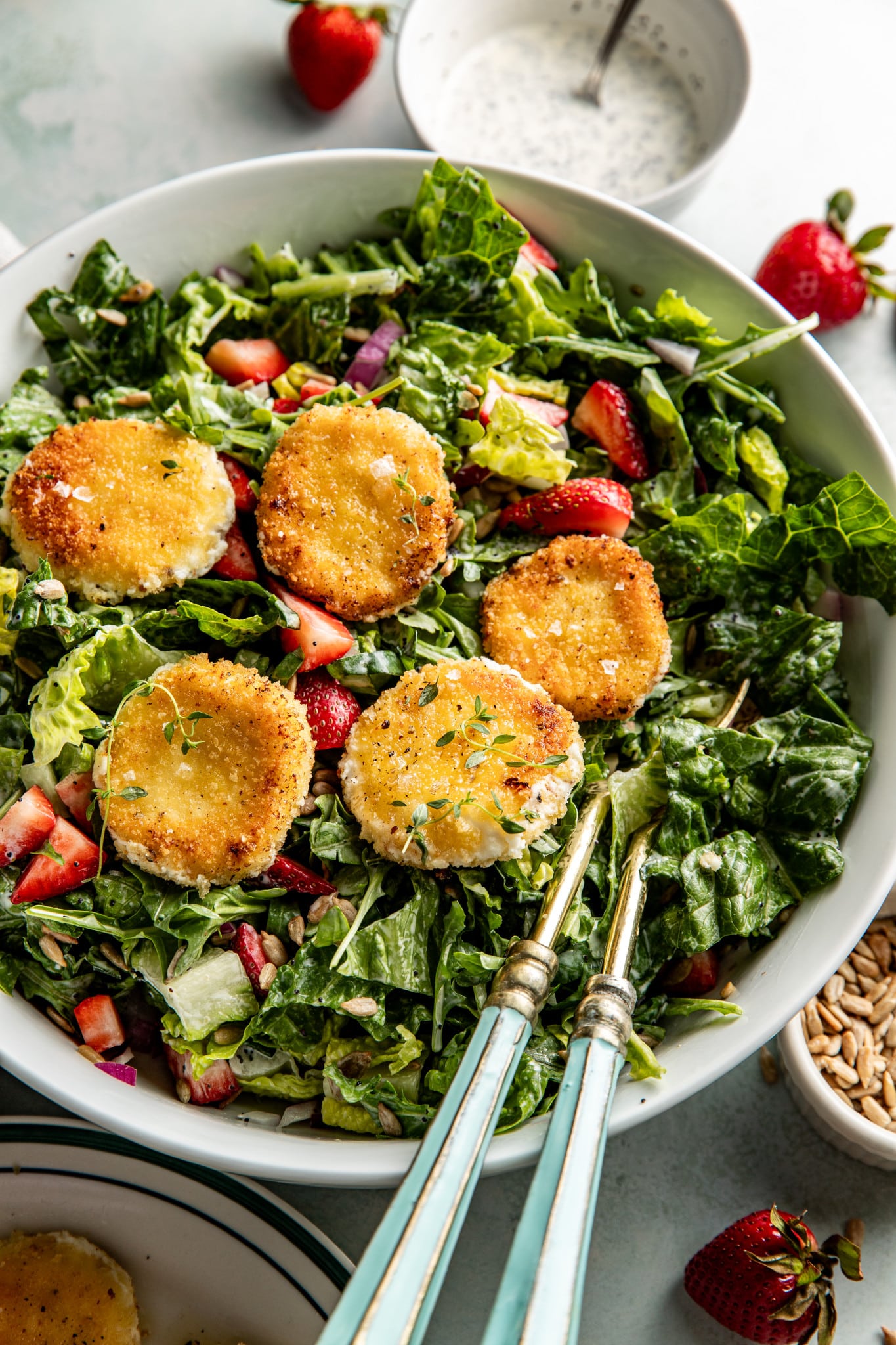 Close-up of the strawberry salad topped with five crispy goat cheese medallions, garnished with thyme and surrounded by dressed greens, strawberries, and seeds.

