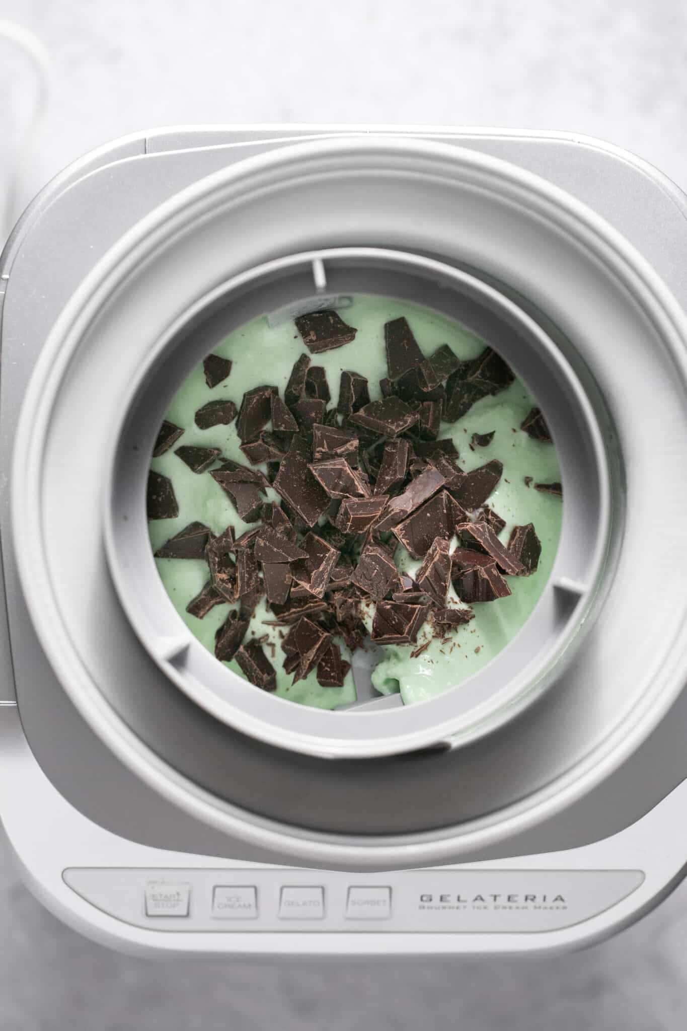 ice cream being churned in an ice cream maker with chocolate chunks on top. 