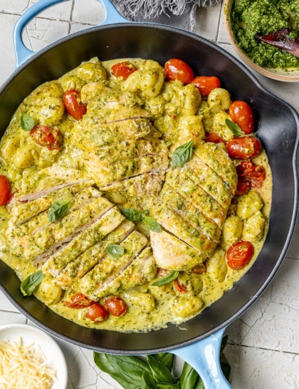 cast iron skillet with sliced chicken breast and cherry tomatoes covered in pesto sauce