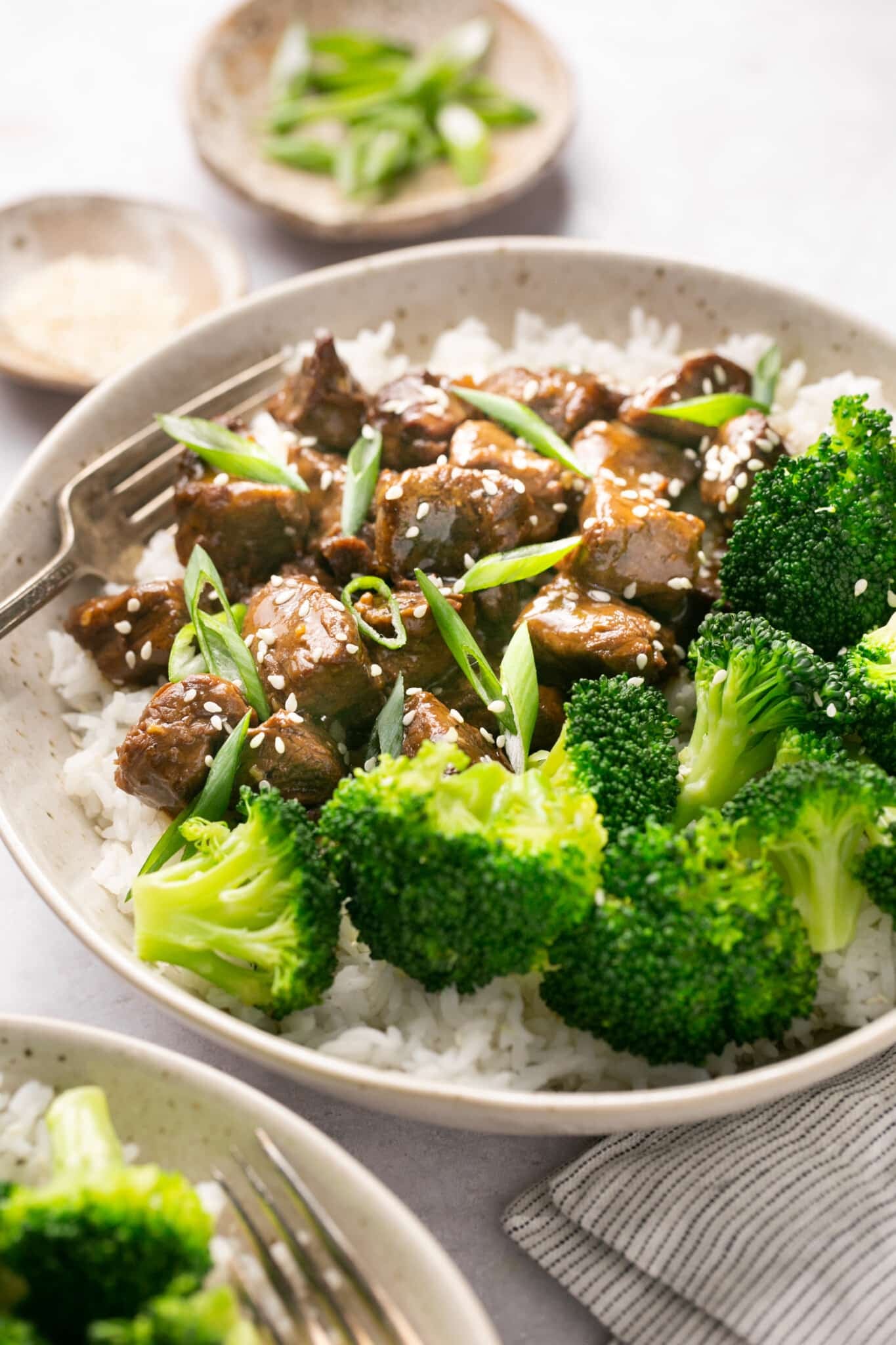 steak bites in a bowl over with with broccoli and garnished with green onions and sesame seeds. 