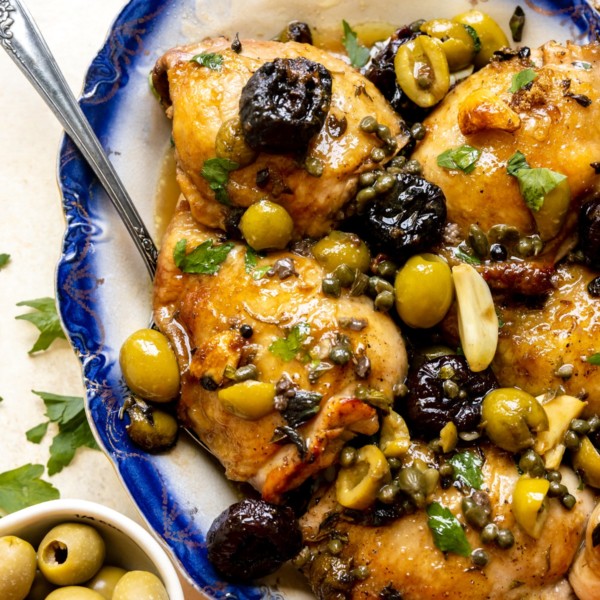chicken thighs with green and black olives and spices on a blue plate