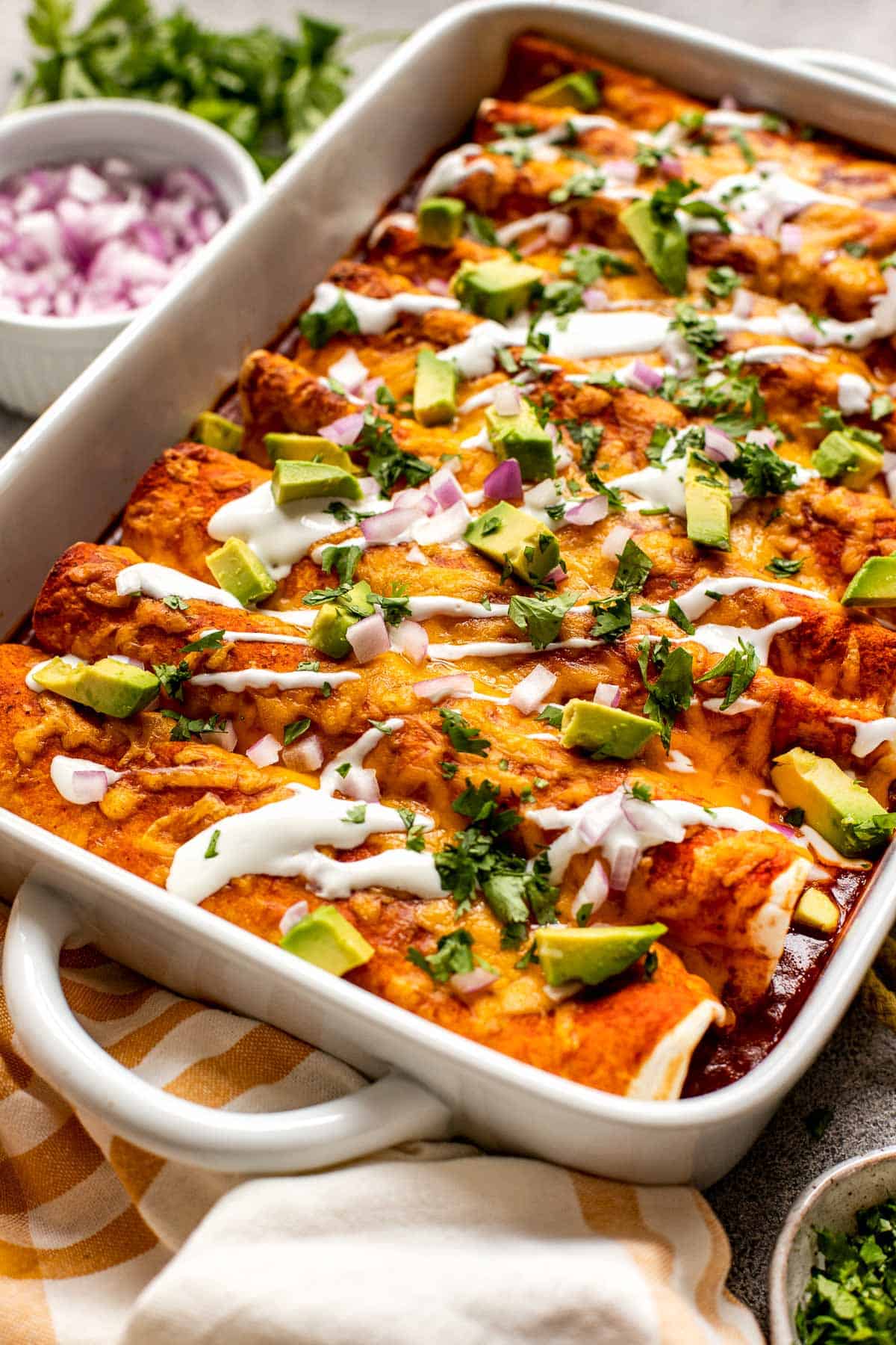 enchiladas in a white casserole dish garnished with sour cream, avocado and red onion. 