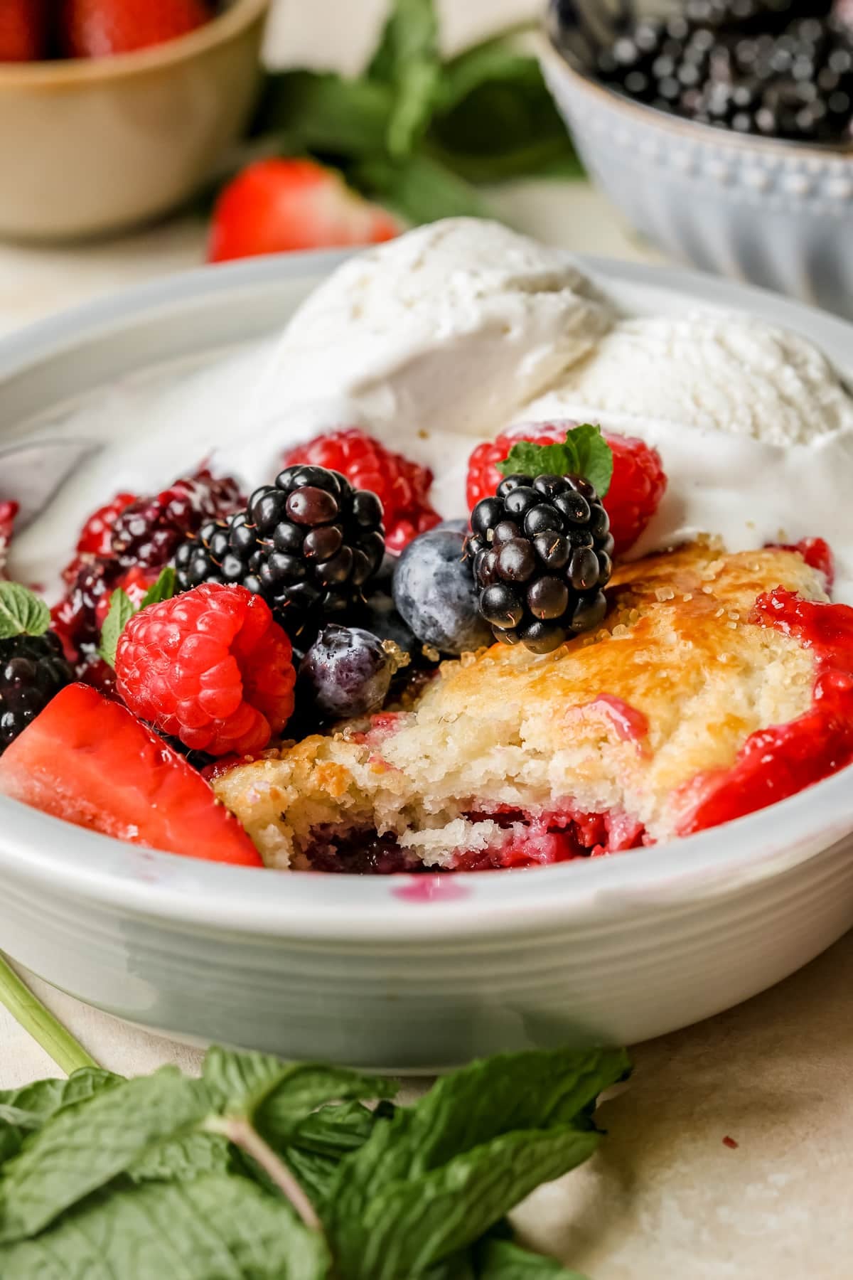 cobbler in a blue bowl with fresh berries and ice cream on top. 