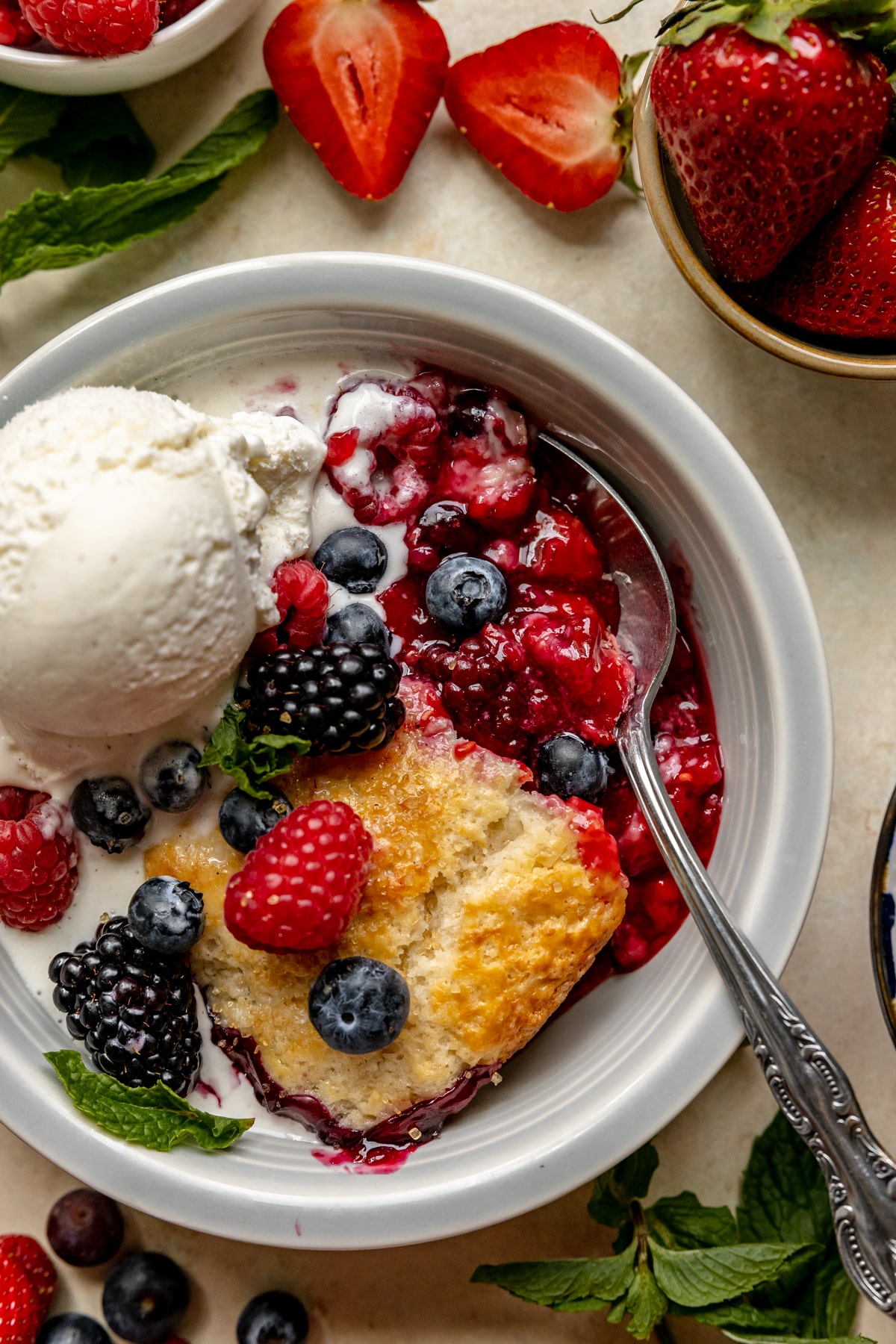 cobbler in a blue bowl with fresh berries and ice cream on top. 