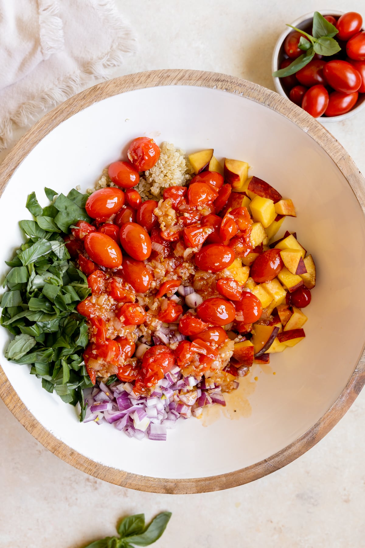 peaches, basil, red onion, quinoa and cherry tomato vinaigrette in a large white salad bowl. 