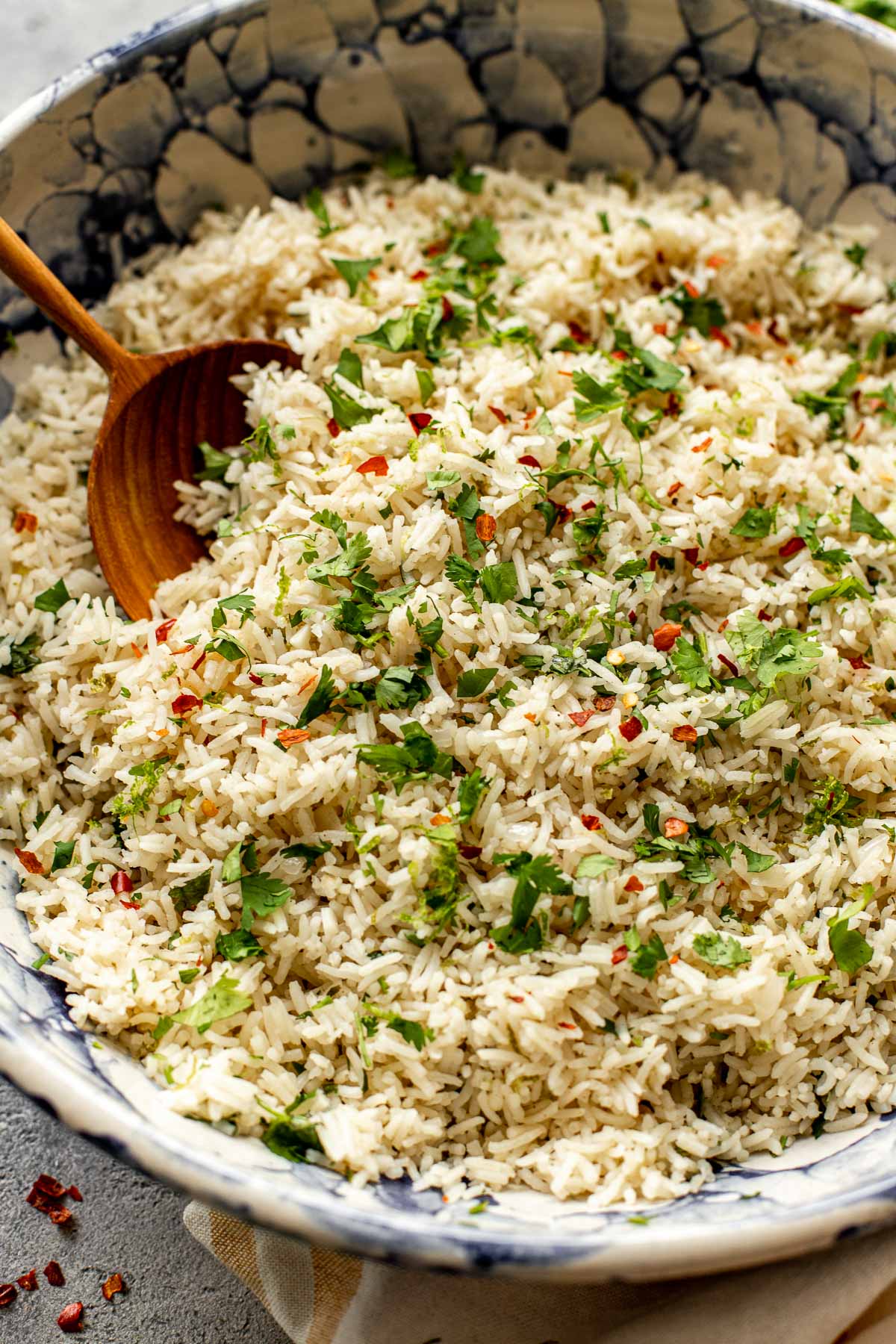 Rice in a blue and white bowl with a wooden spoon garnished with cilantro and red pepper chili flakes. 