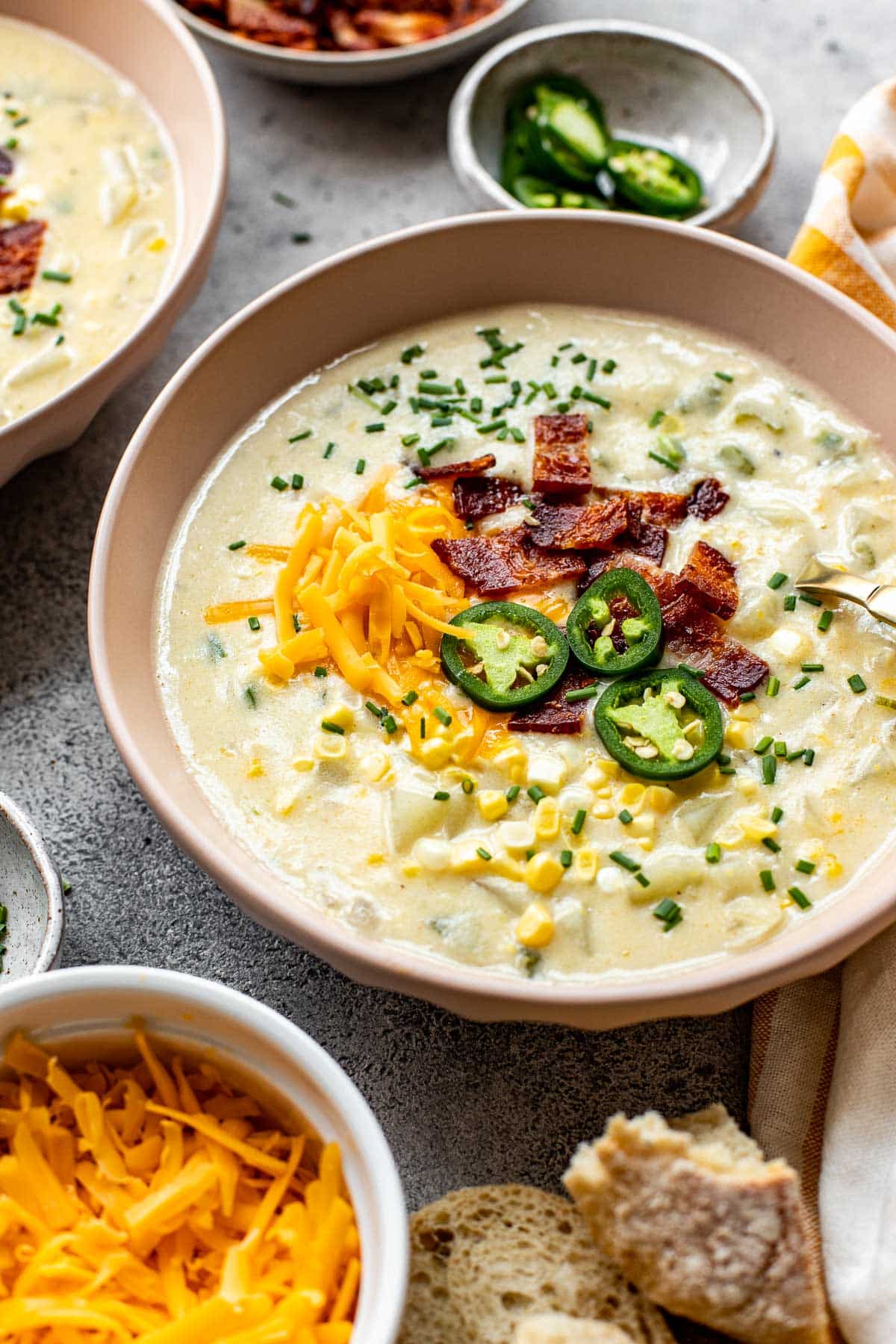 corn chowder in a pink bowl garnished with bacon, cheddar and jalapeno