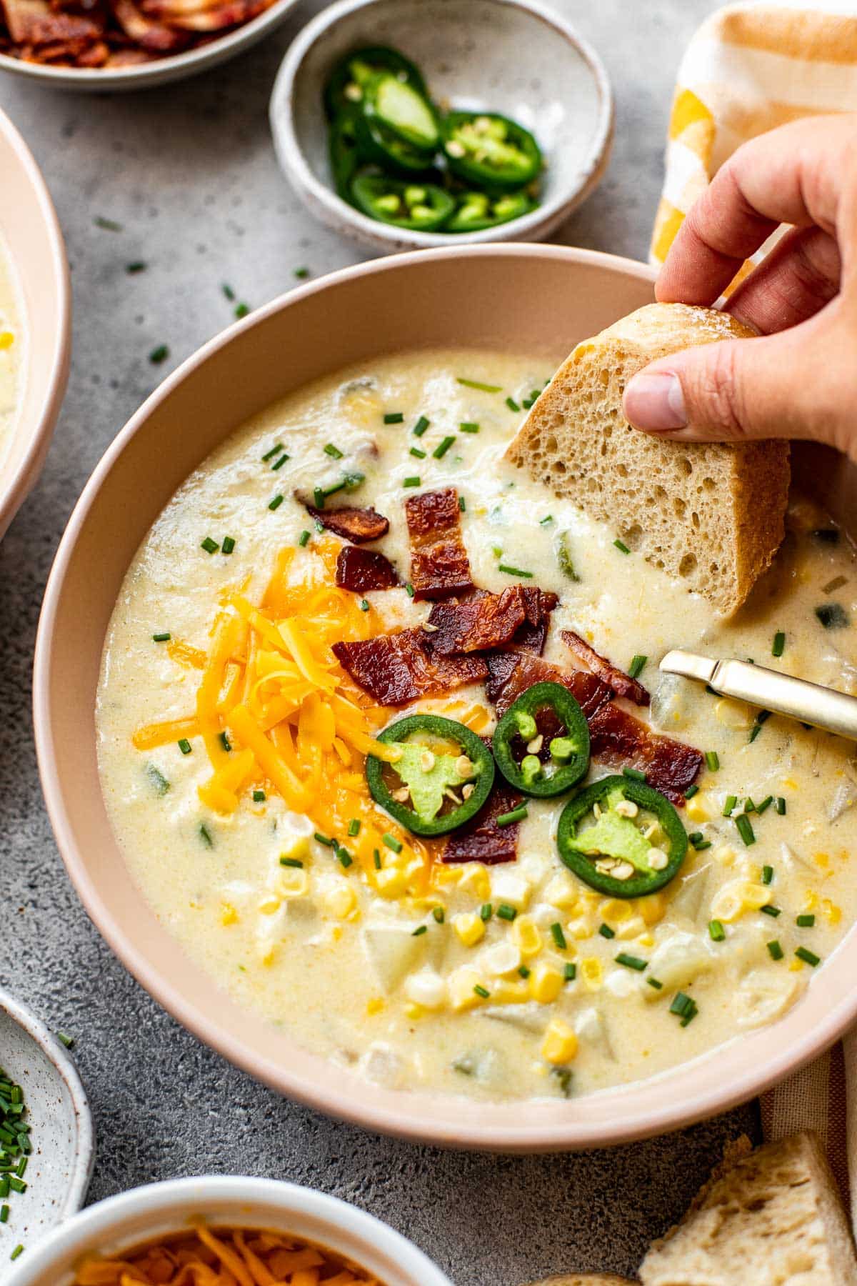 a hand dunking some bread into a bowl of corn chowder. 