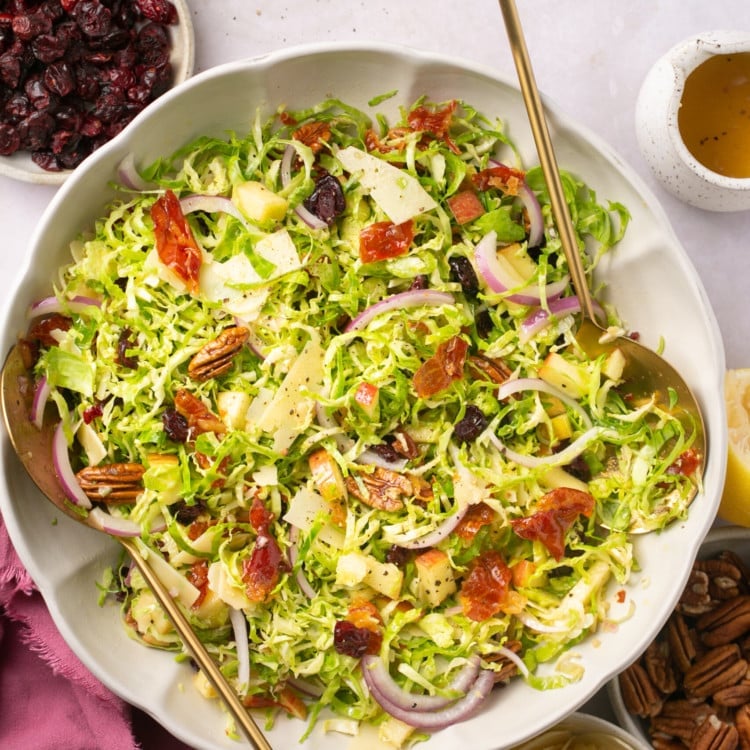 shaved brussel sprouts, pecans, red onions, apple slices, bacon crumbles, shredded parmesan mixed as a salad in a white bowl