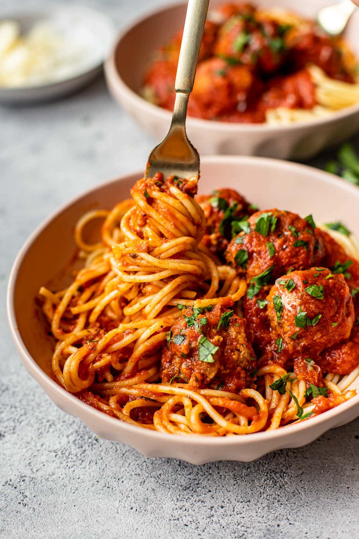 A fork twirling spaghetti noodles with meatballs on the side garnished with parsley. 