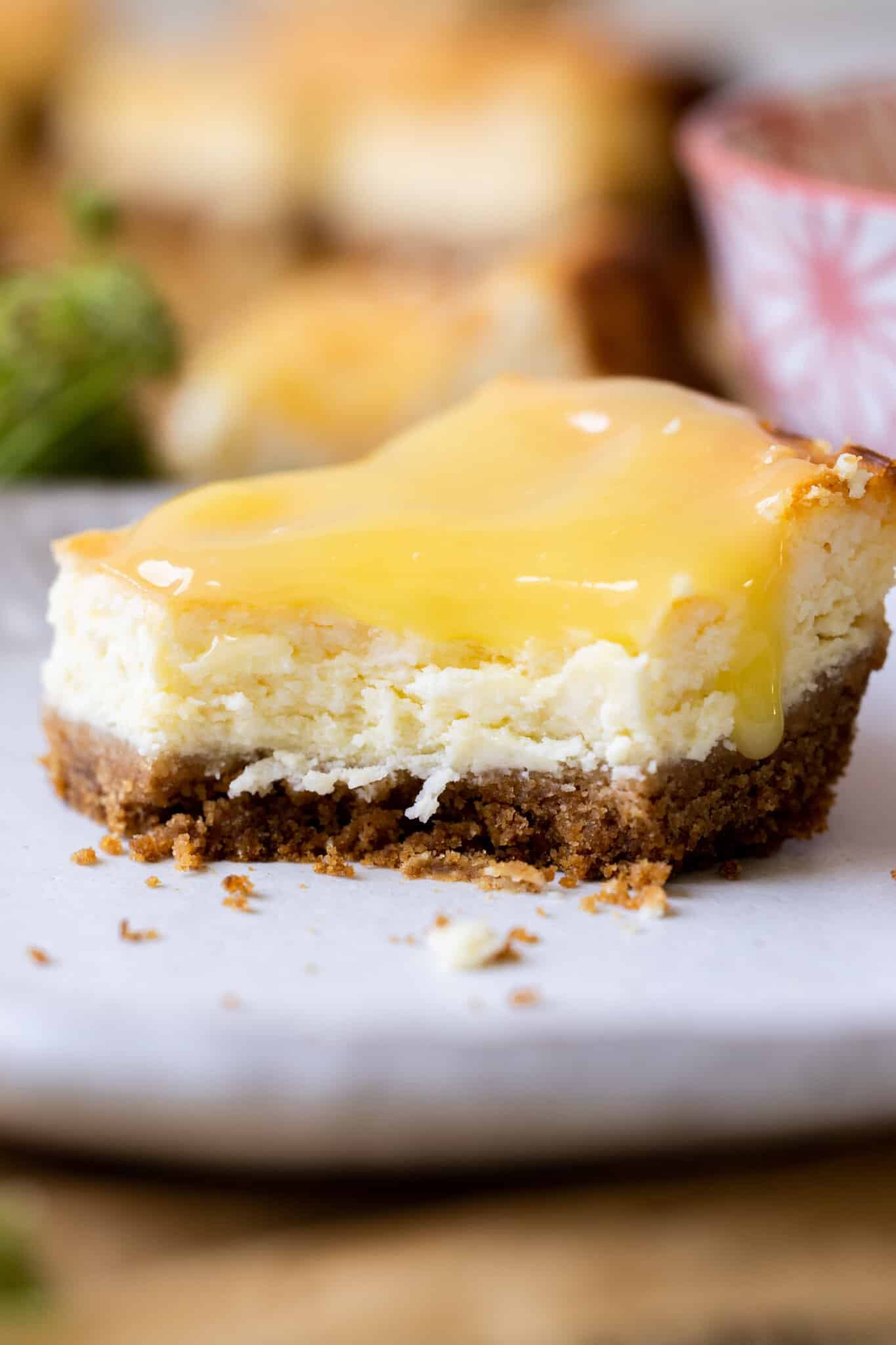 cheesecake on a white plate with a bite taken out of it with lemon curd on top.