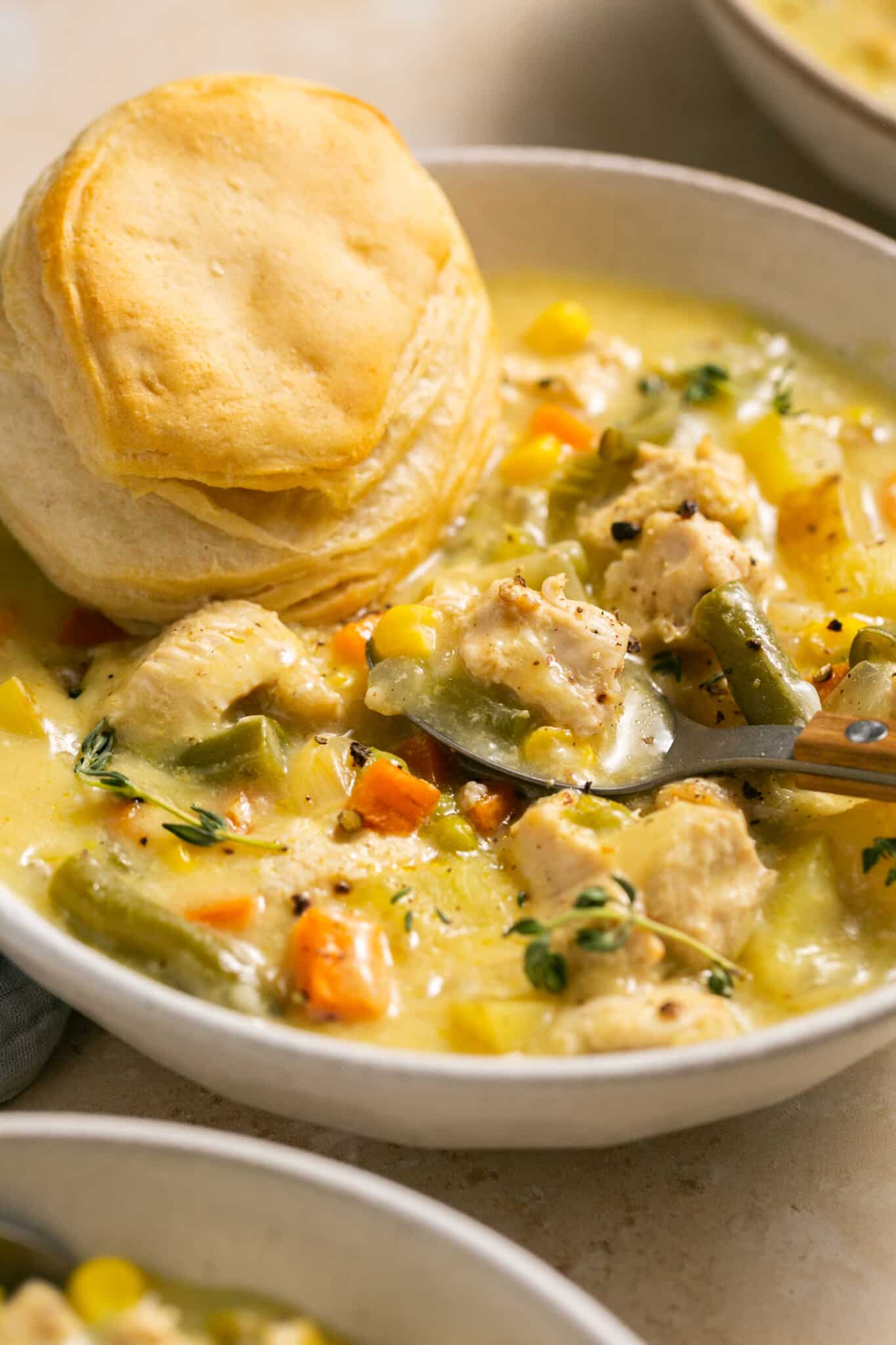 a bowl filled with soup with a spoon taking a bite and a biscuit on the side.