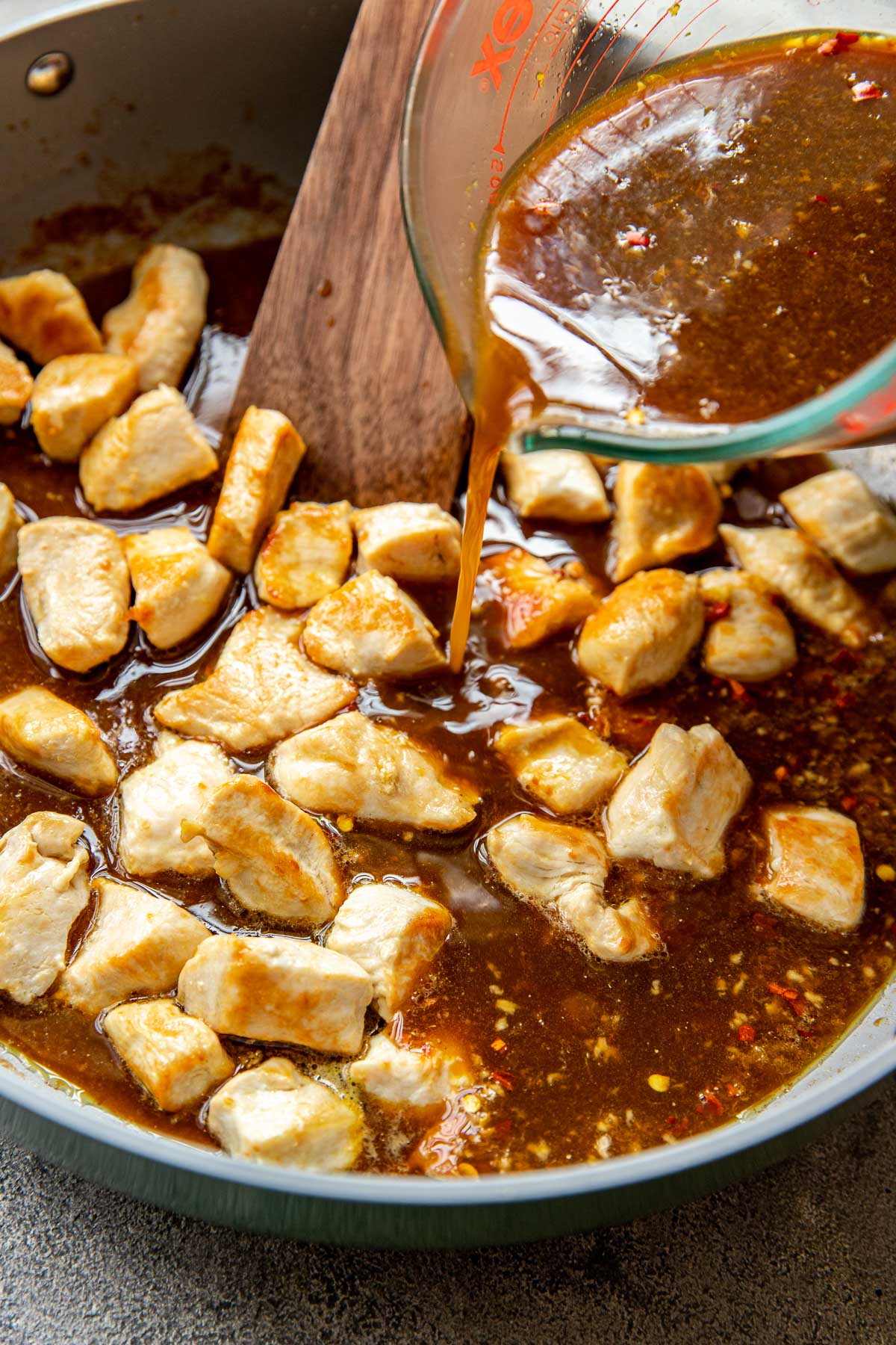 sauce being poured onto chicken in a skillet. 