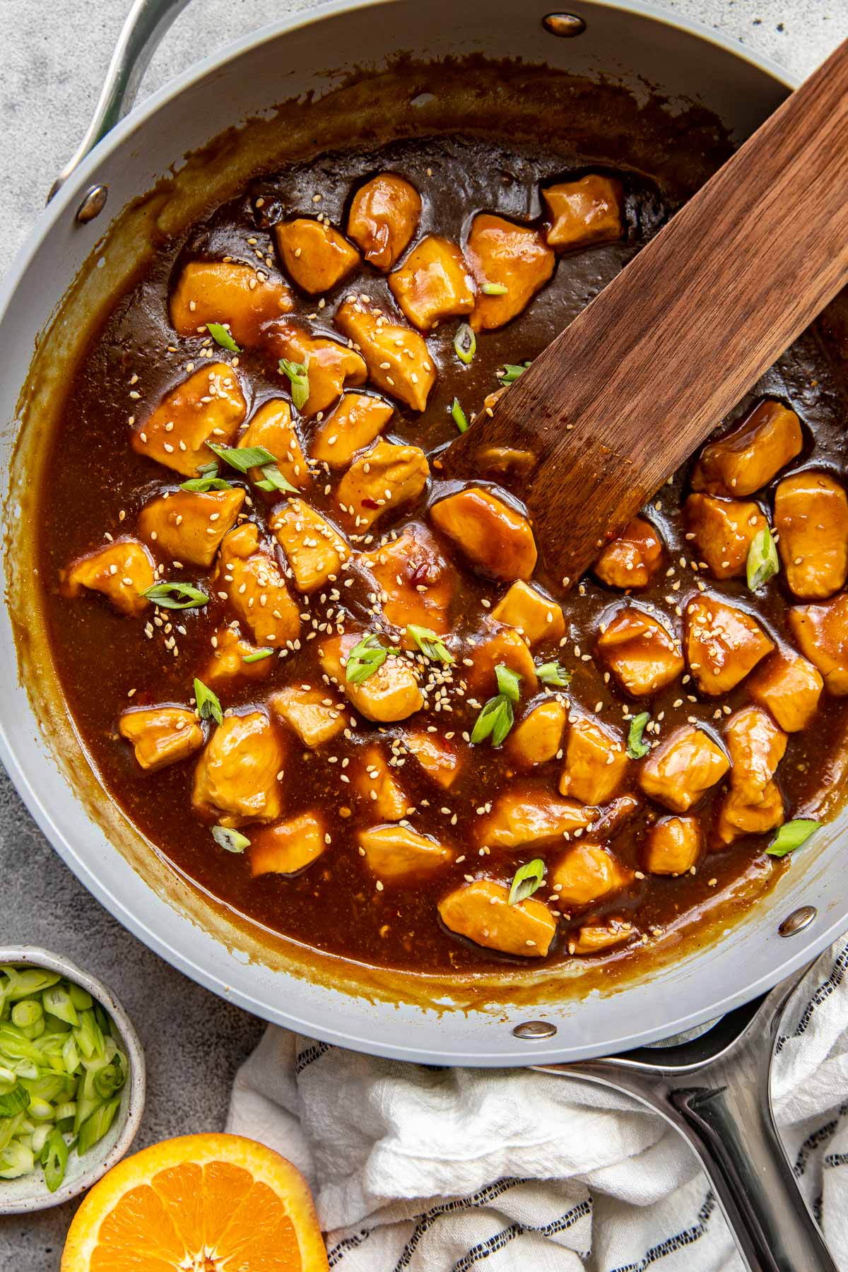 orange chicken garnished with green onions and sesame seeds in a skillet. 