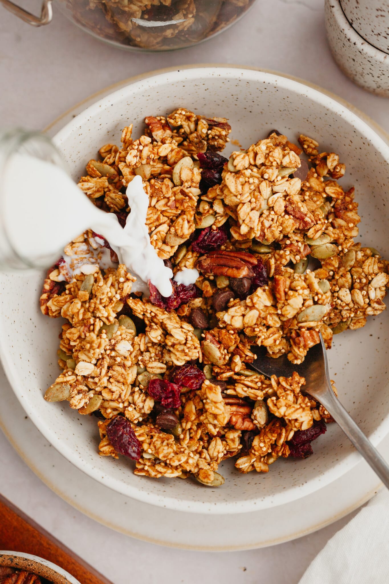 milk being poured onto granola in a white speckled bowl. 