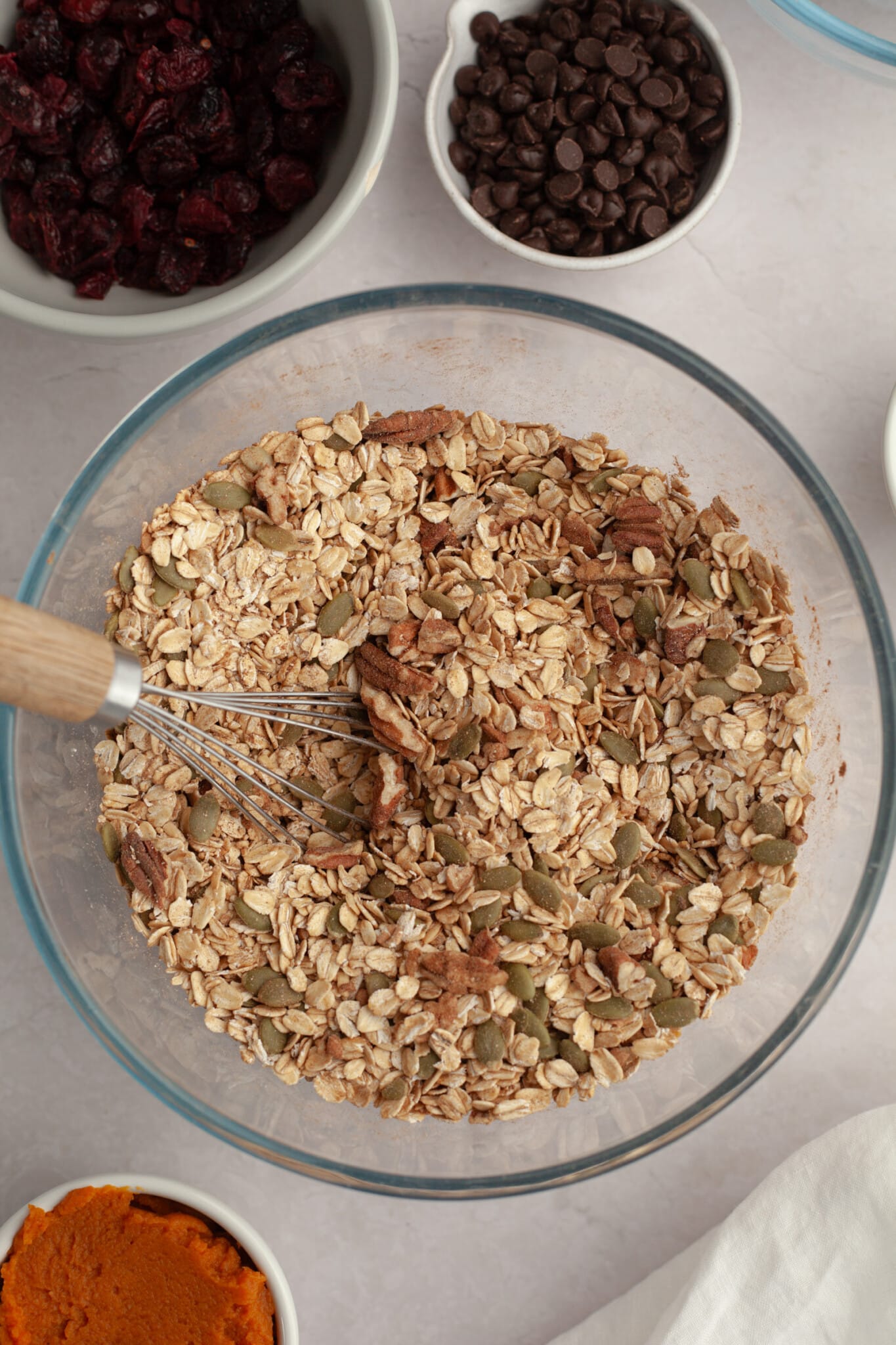 oats, pecans and pepitas in a glass bowls with a whisk. 