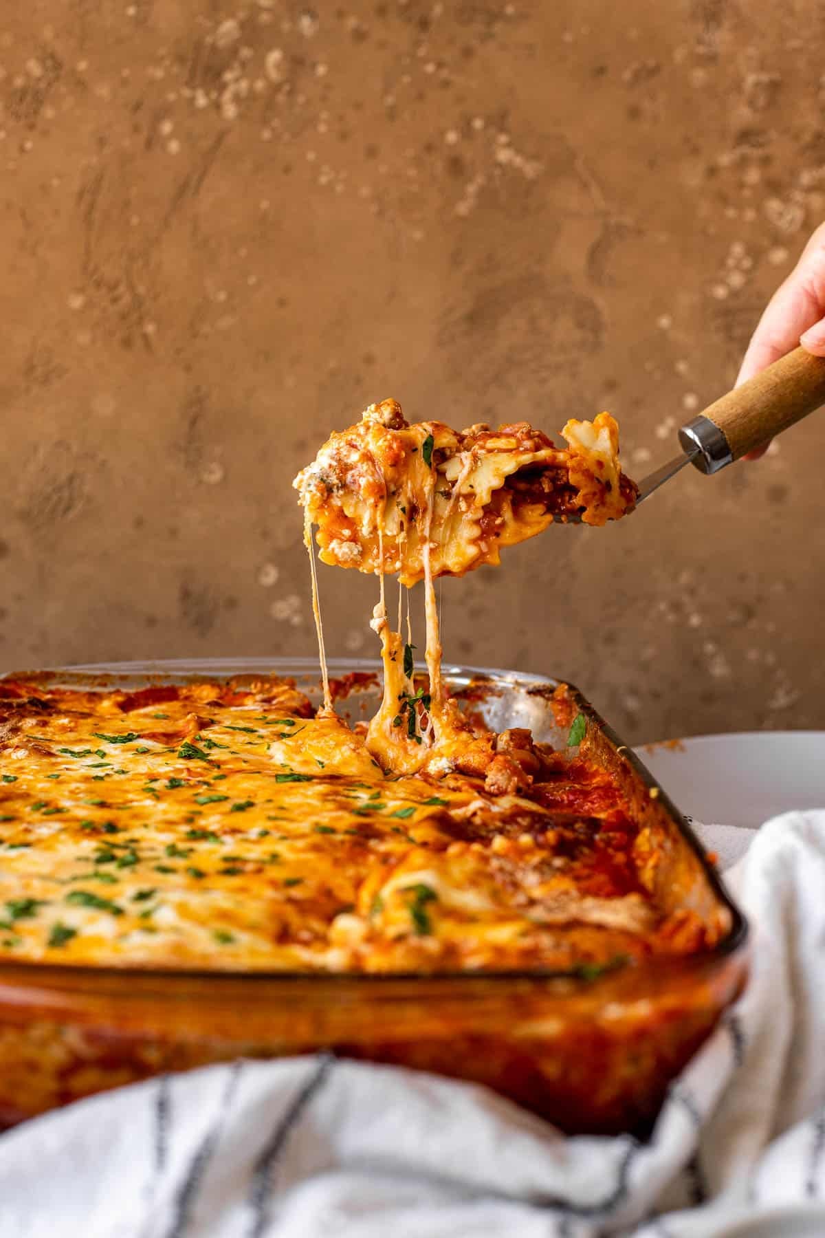 Ravioli lasagna being served from a baking dish with a cheesy pull. 