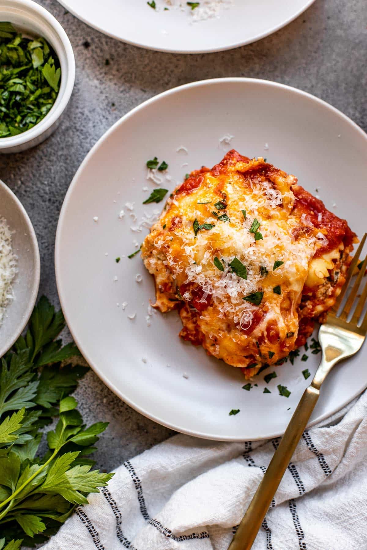 Ravioli lasagna on a plate with Parmesan on top and parsley. 