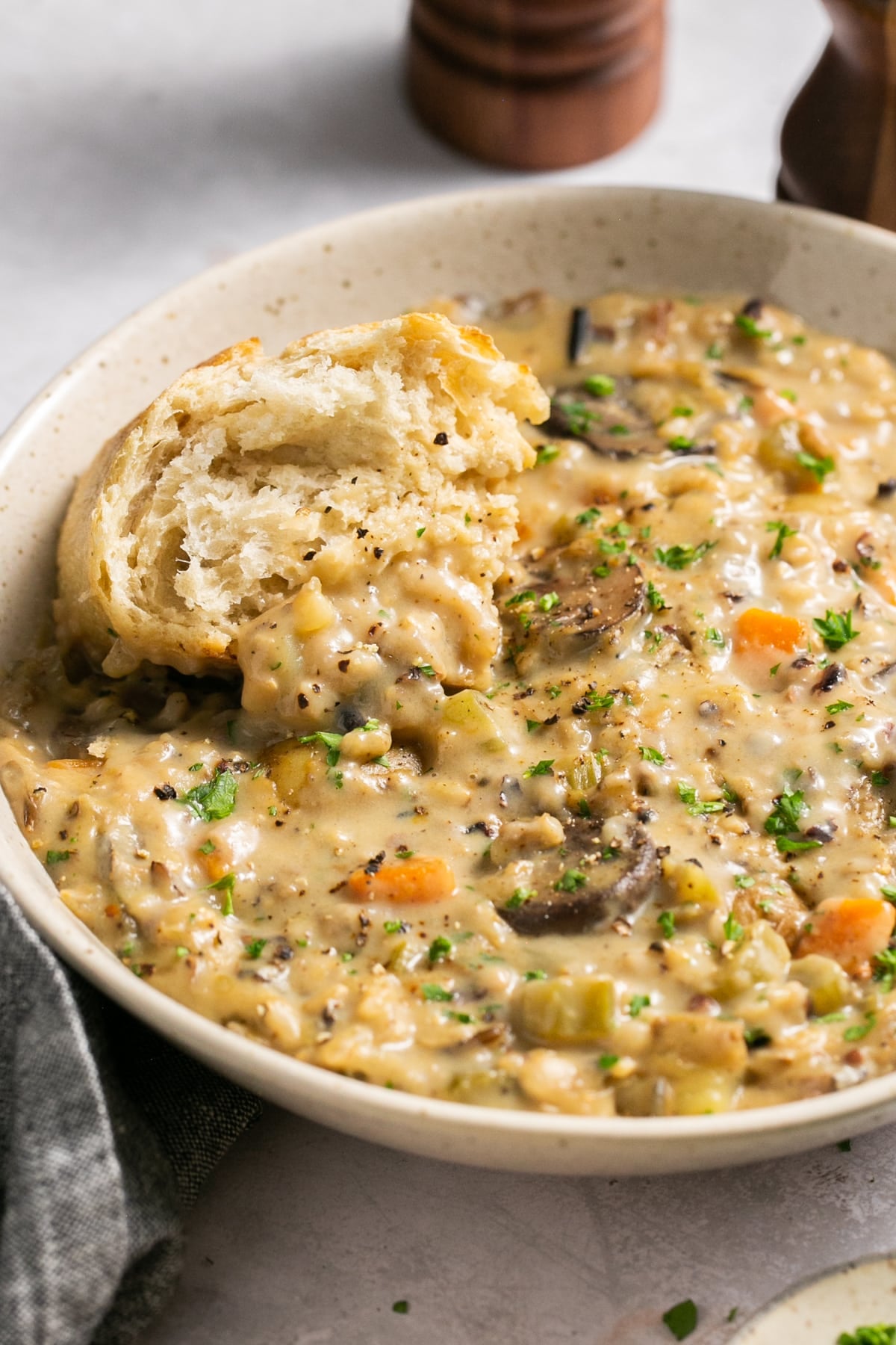 creamy wild rice soup in a bowl with crusty bread dunking in it.