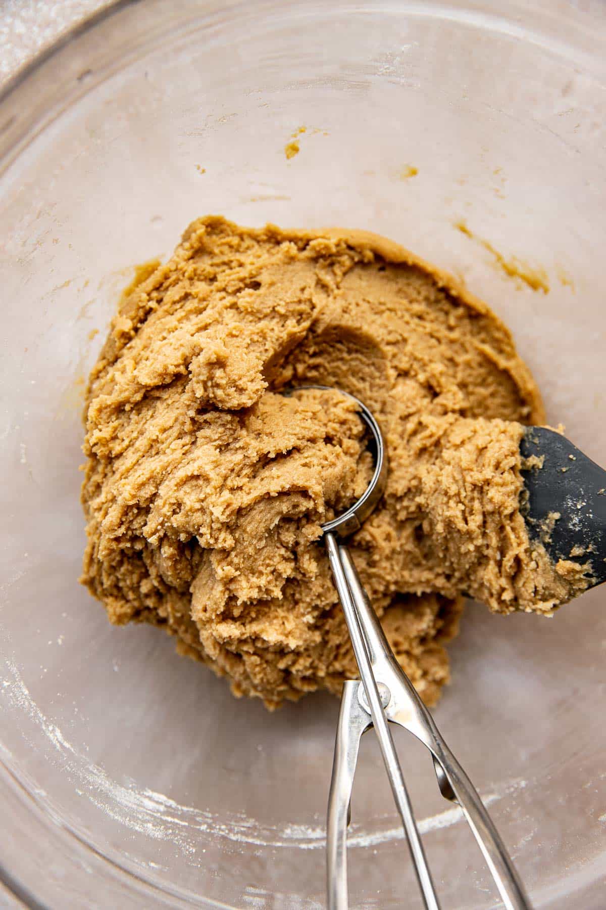 a cookie scoop scooping cookie dough out of a glass mixing bowl. 