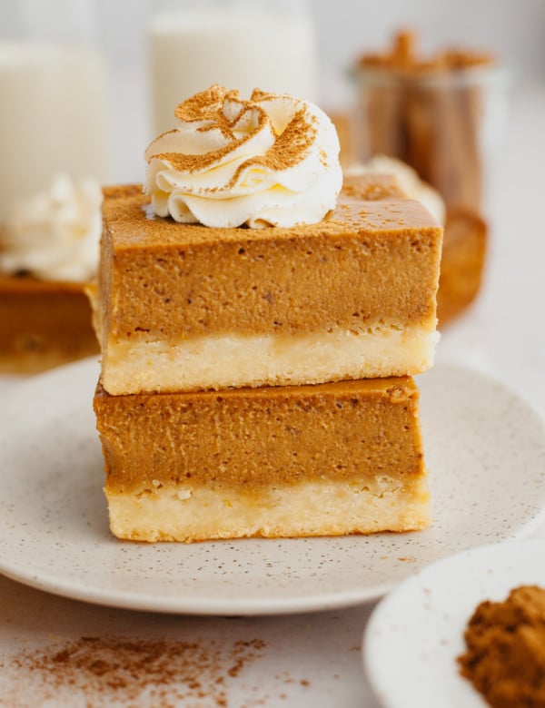 two pumpkin pie bars stacked on a tan plate and topped with a whipped cream swirl