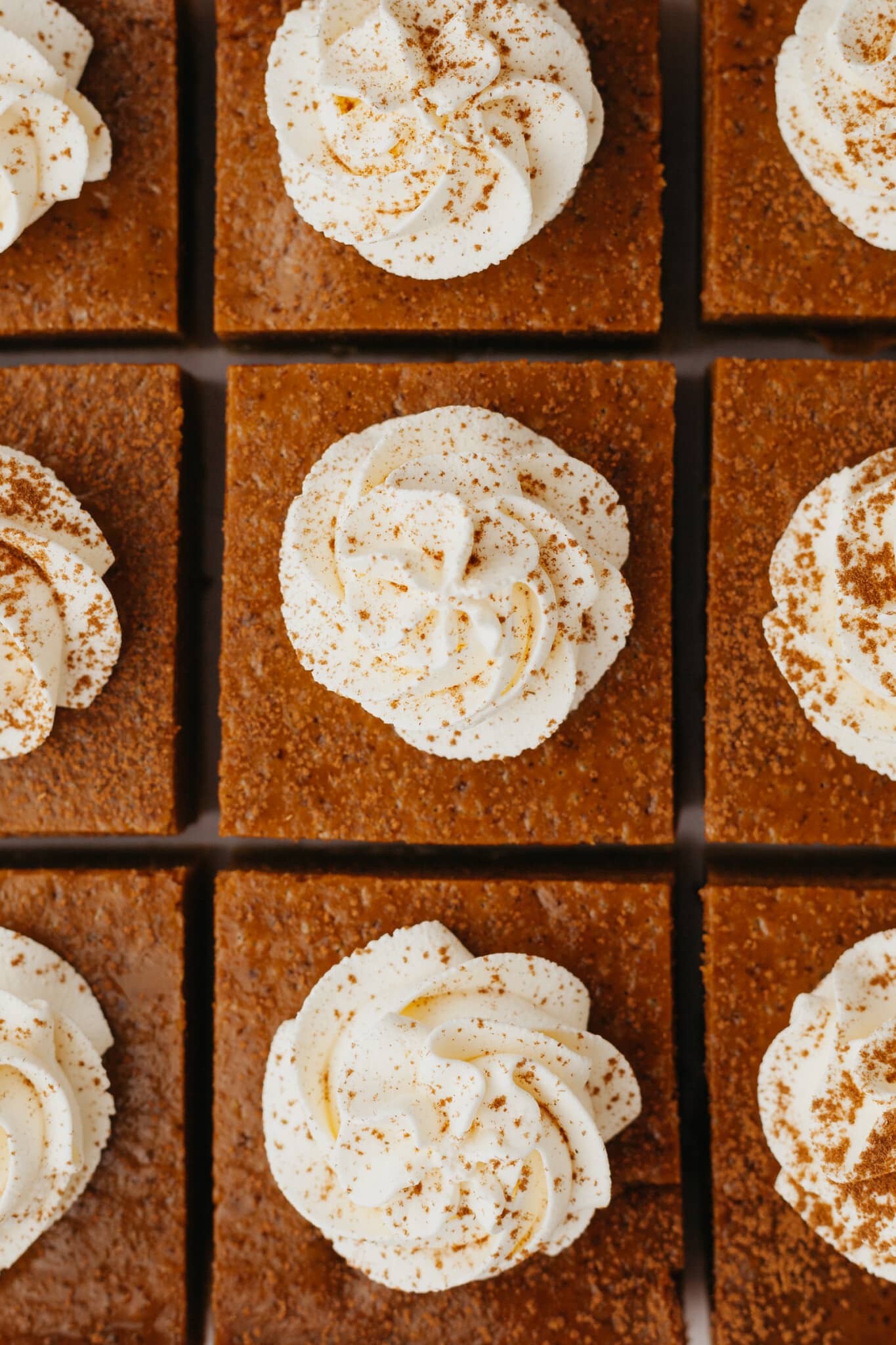 a close up image of pumpkin pie bars garnished with whipped cream and sprinkled with cinnamon.