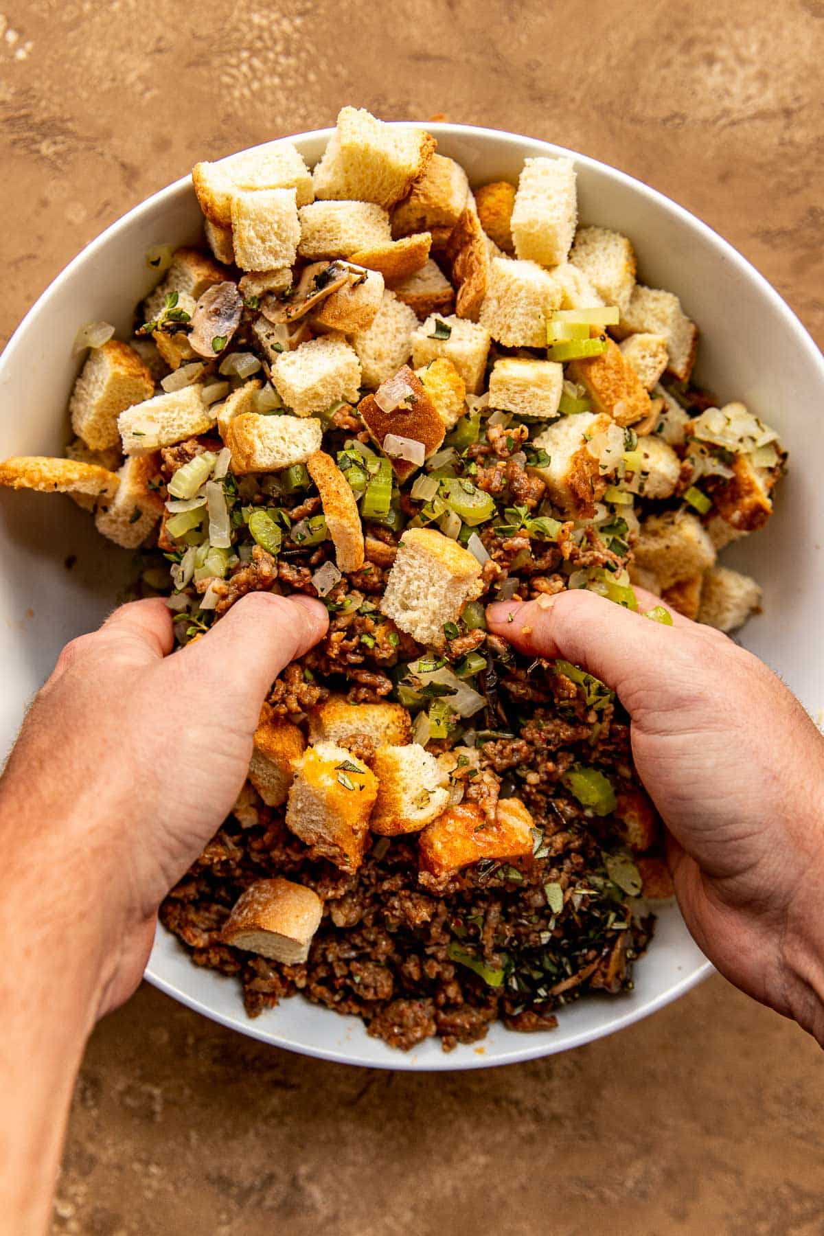 stuffing being mixed with hands in a big white glass bowl. 