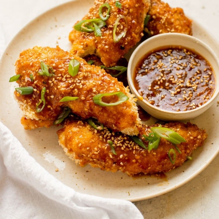 plate with breaded chicken tenders topped with green onions and a side of sauce
