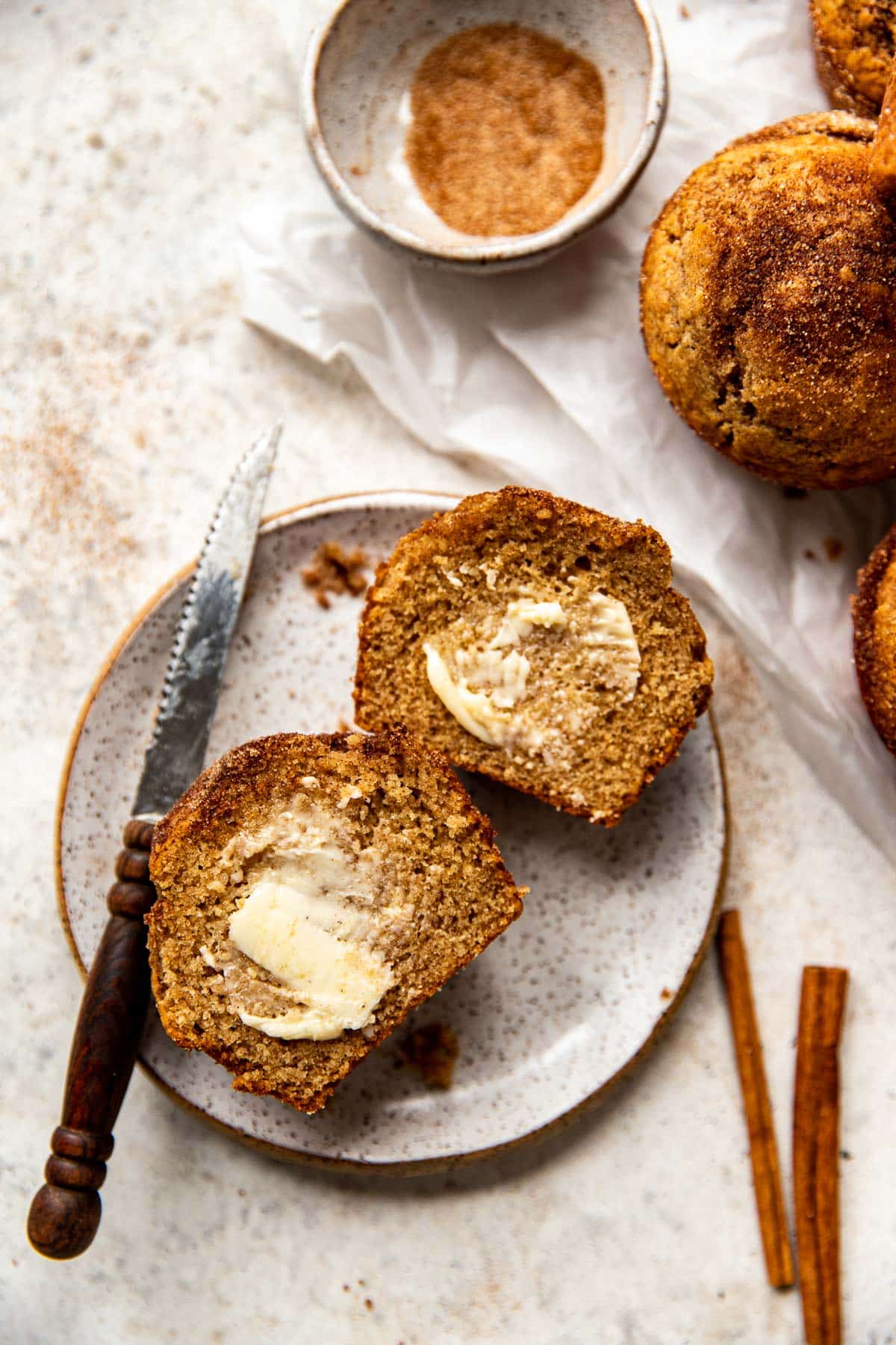 butter brushed on top of a snickerdoodle muffin on a white speckled plate. 