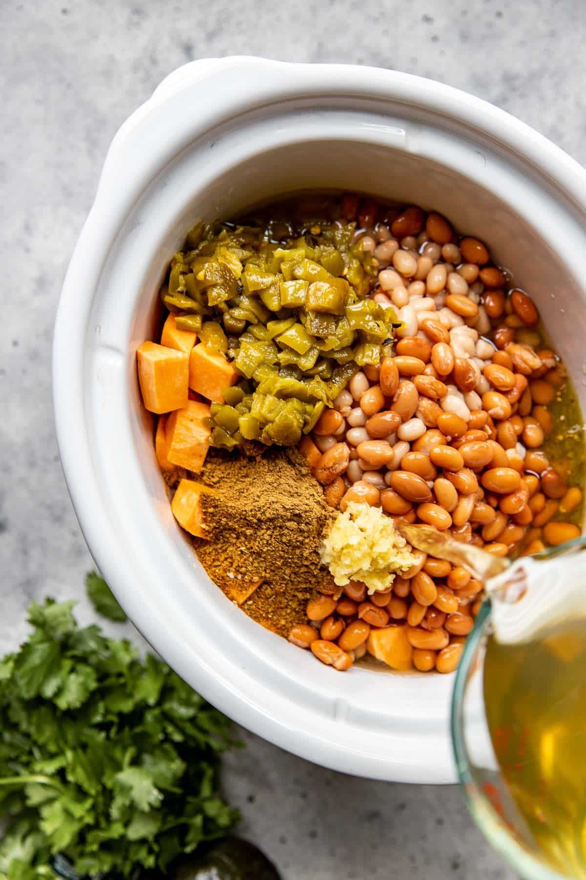ingredients being poured into a white crockpot for chicken chili. 