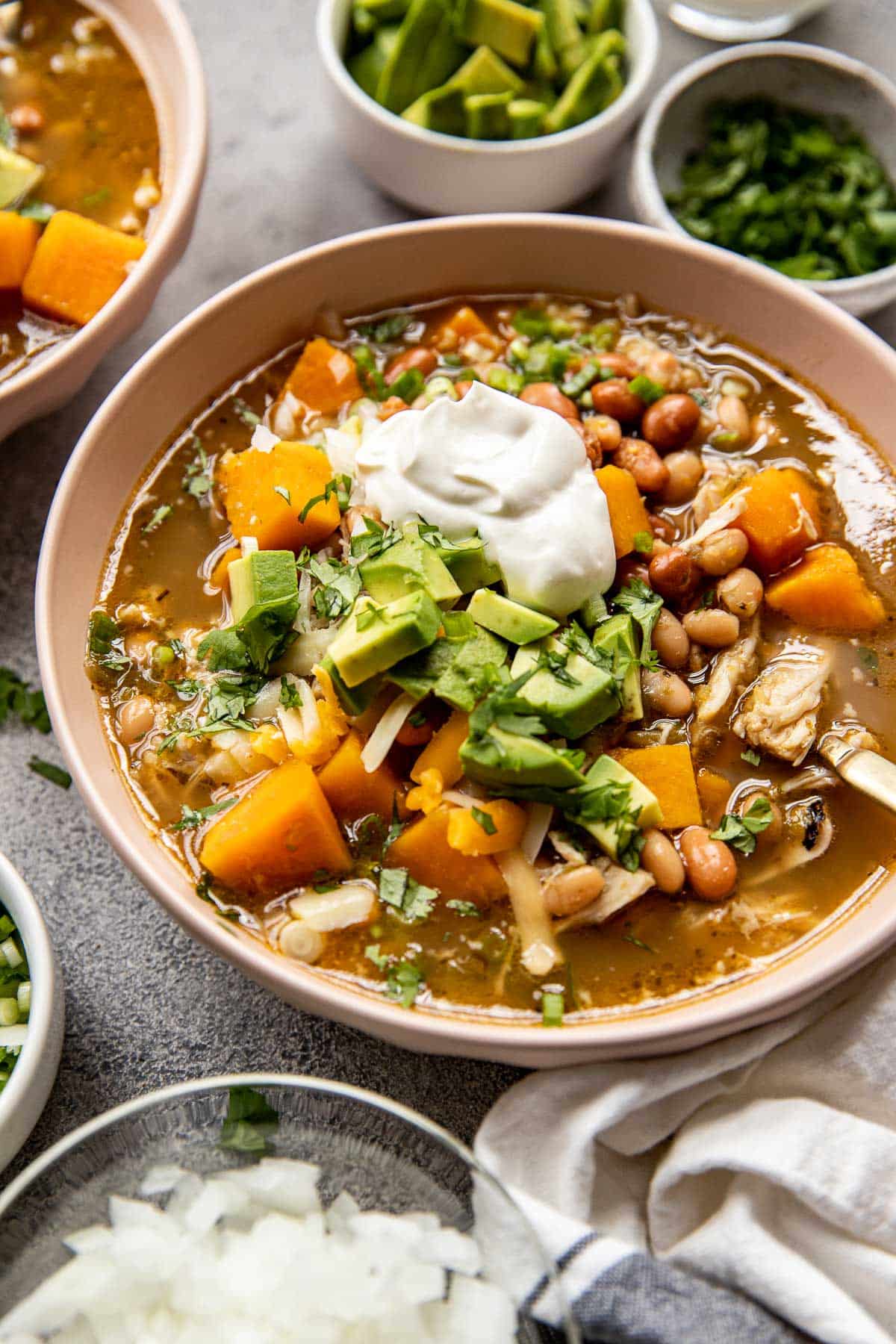 chicken chili in a pink bowl garnished with sour cream, avocado, cilantro. 