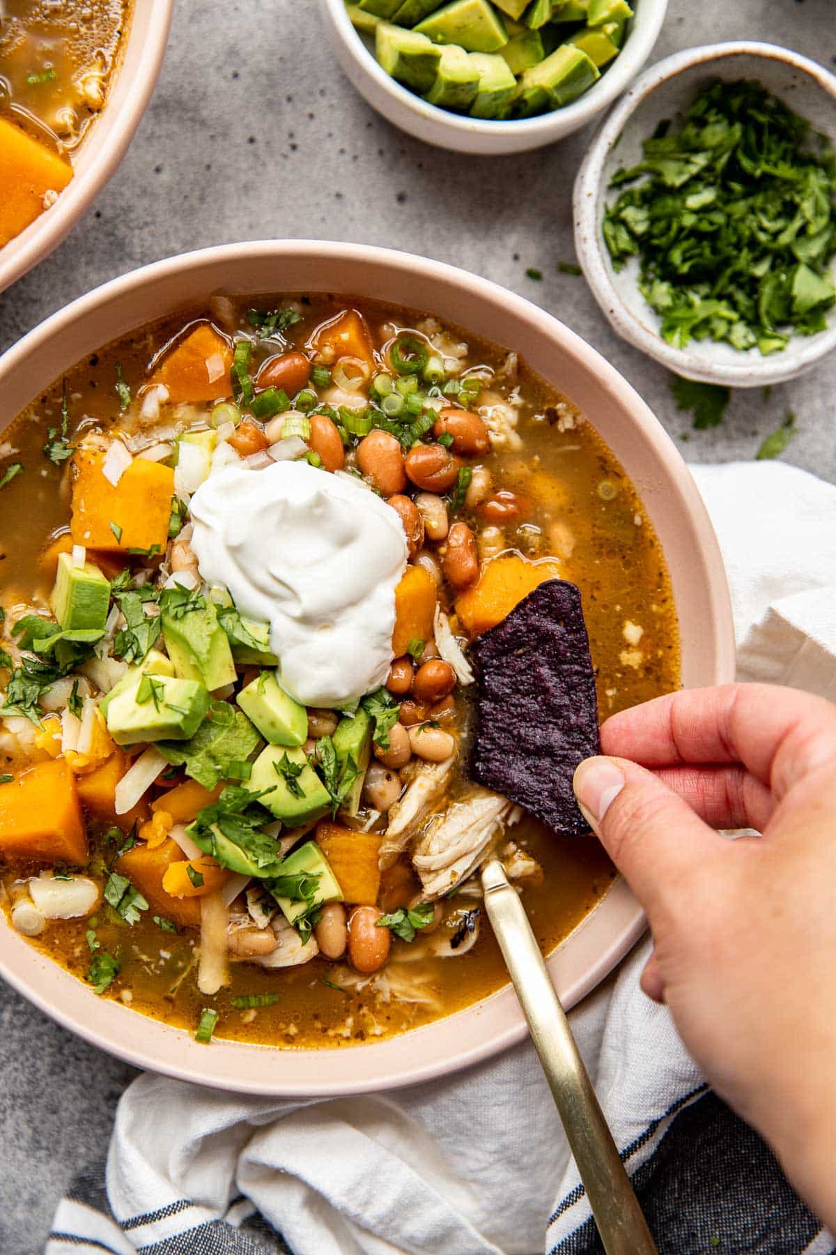 green chicken chili soup in a bowl with a womans hand dipping a chip in the chili. 