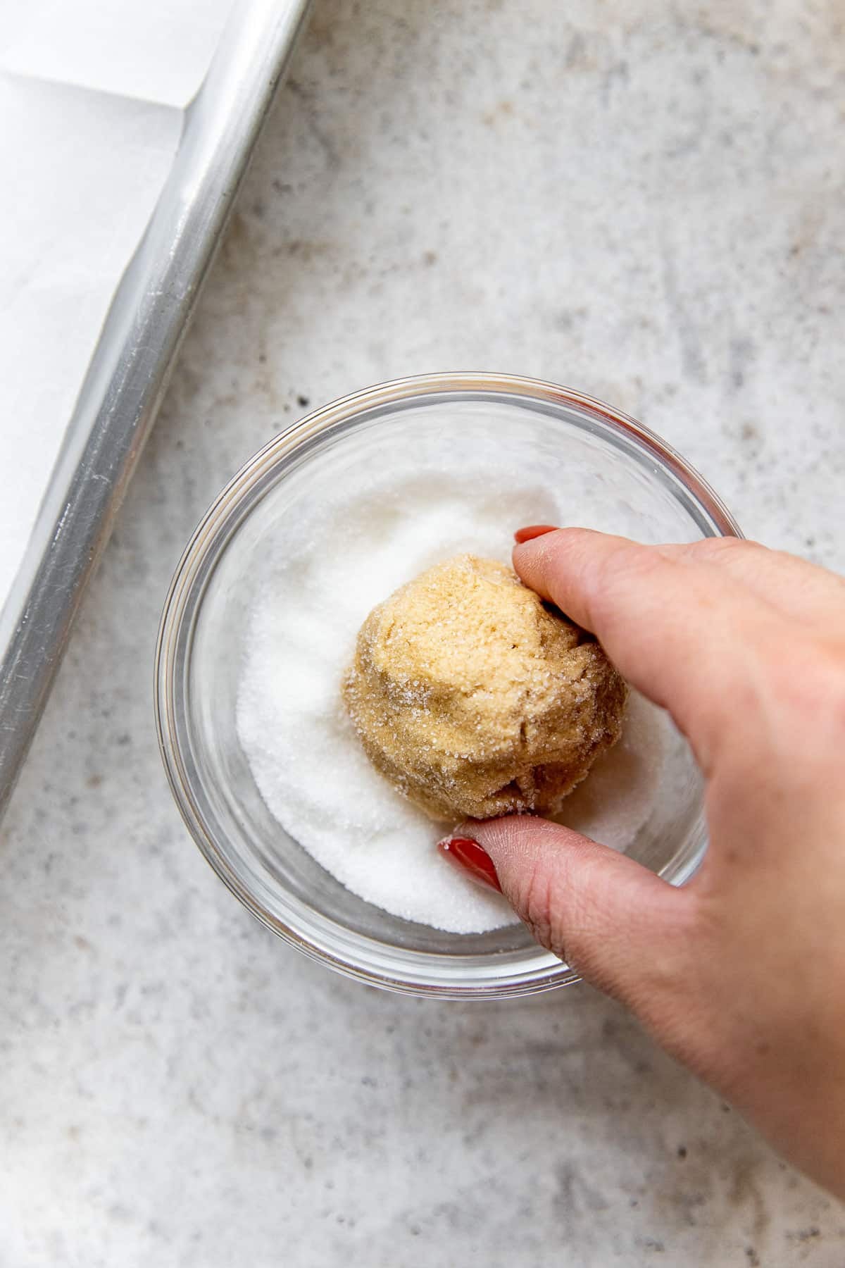 a womans hand rolling peanut butter cookie dough in granulated sugar. 