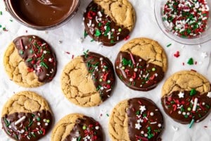 parchment paper with peanut butter cookies half dipped in chocolate with red green and white sprinkles