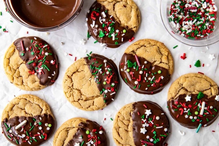 parchment paper with peanut butter cookies half dipped in chocolate with red green and white sprinkles
