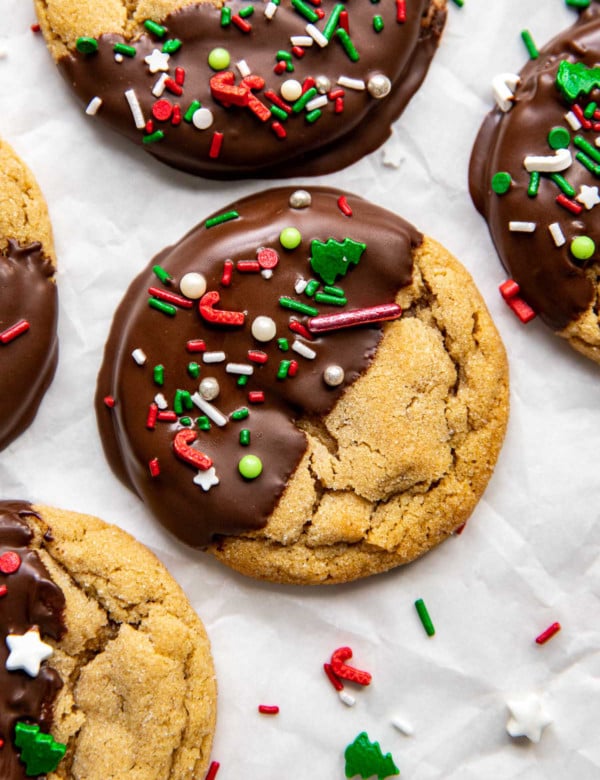 close up of peanut butter cookie half covered with chocolate and white green and red sprinkles