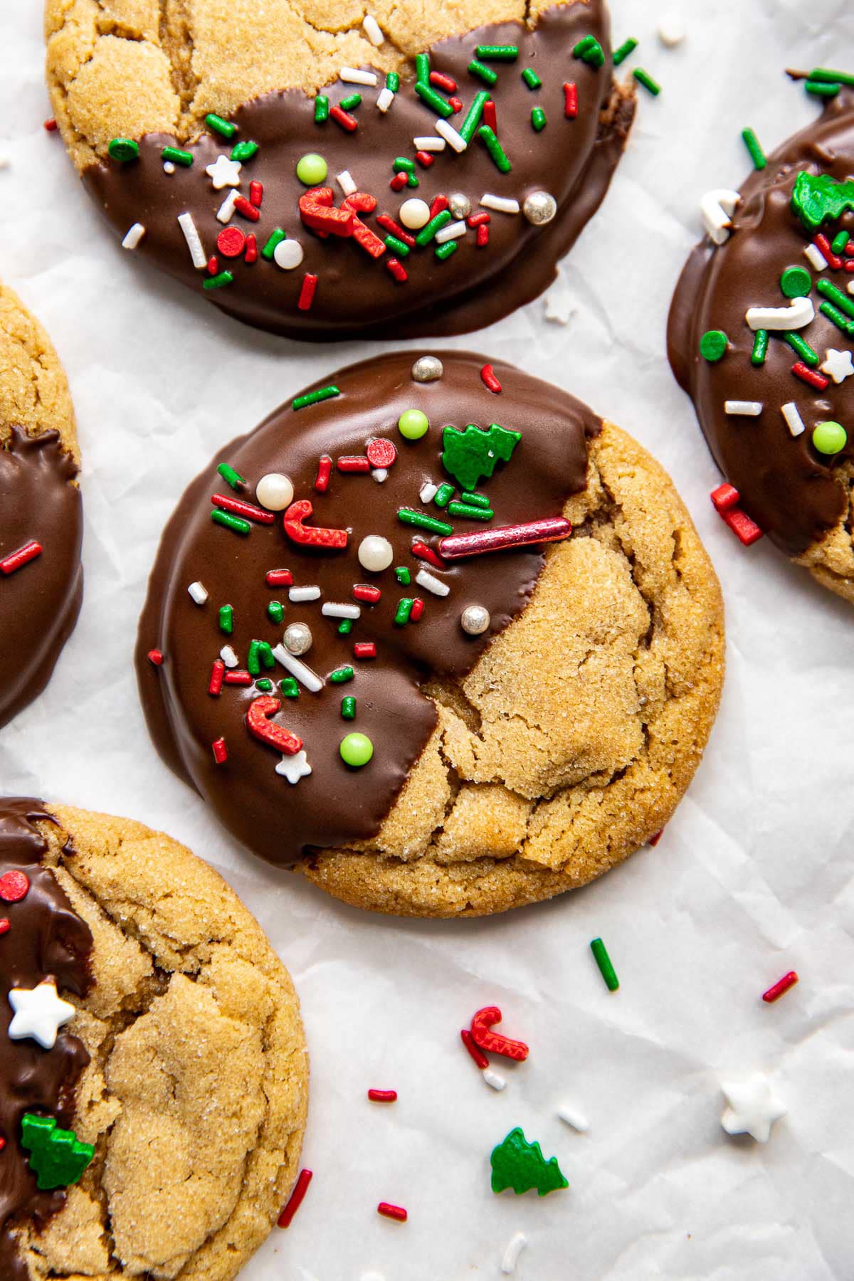 close up of peanut butter cookie half covered with chocolate and white green and red sprinkles
