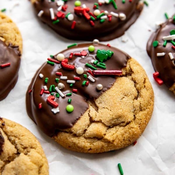 close up of a peanut butter cookie with half dipped in chocolate topped with red white and green sprinkles