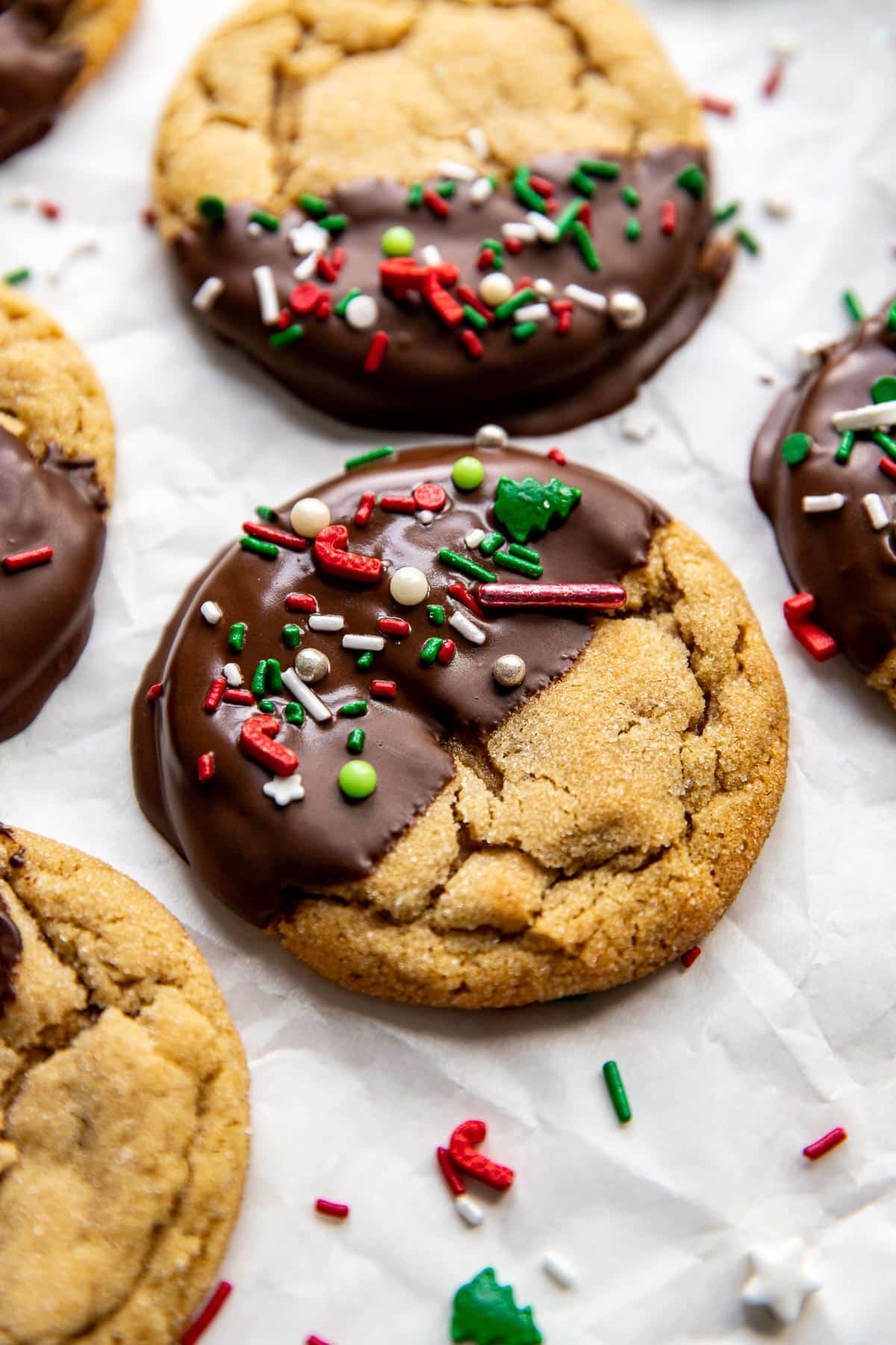 a peanut butter cookie half dipped in dark chocolate and decorated with christmas sprinkles. 