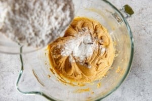 flour being added to wet ingredients in a clear bowl