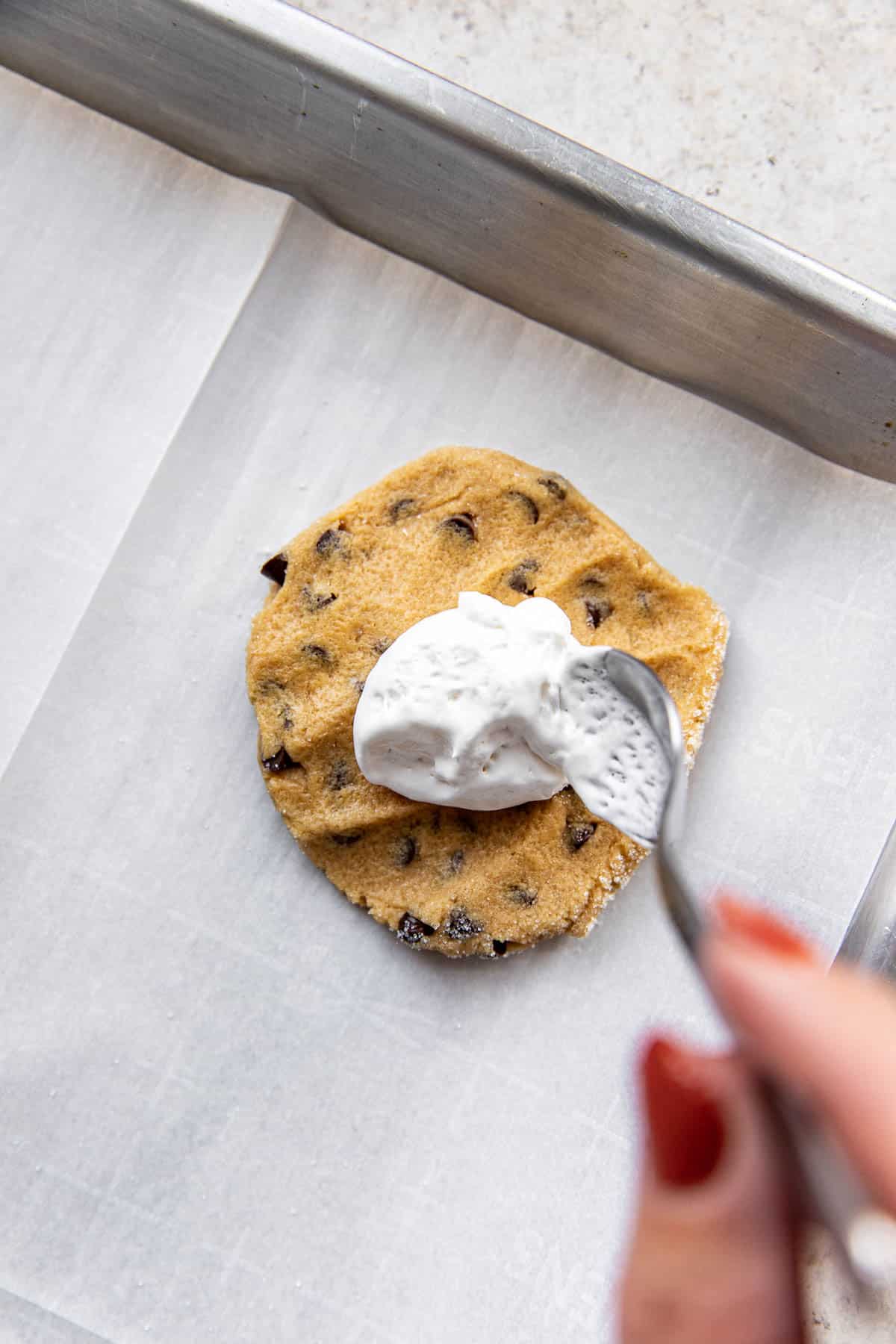 marshmallow fluff being spooned on to a peanut butter chocolate chip cookie. 