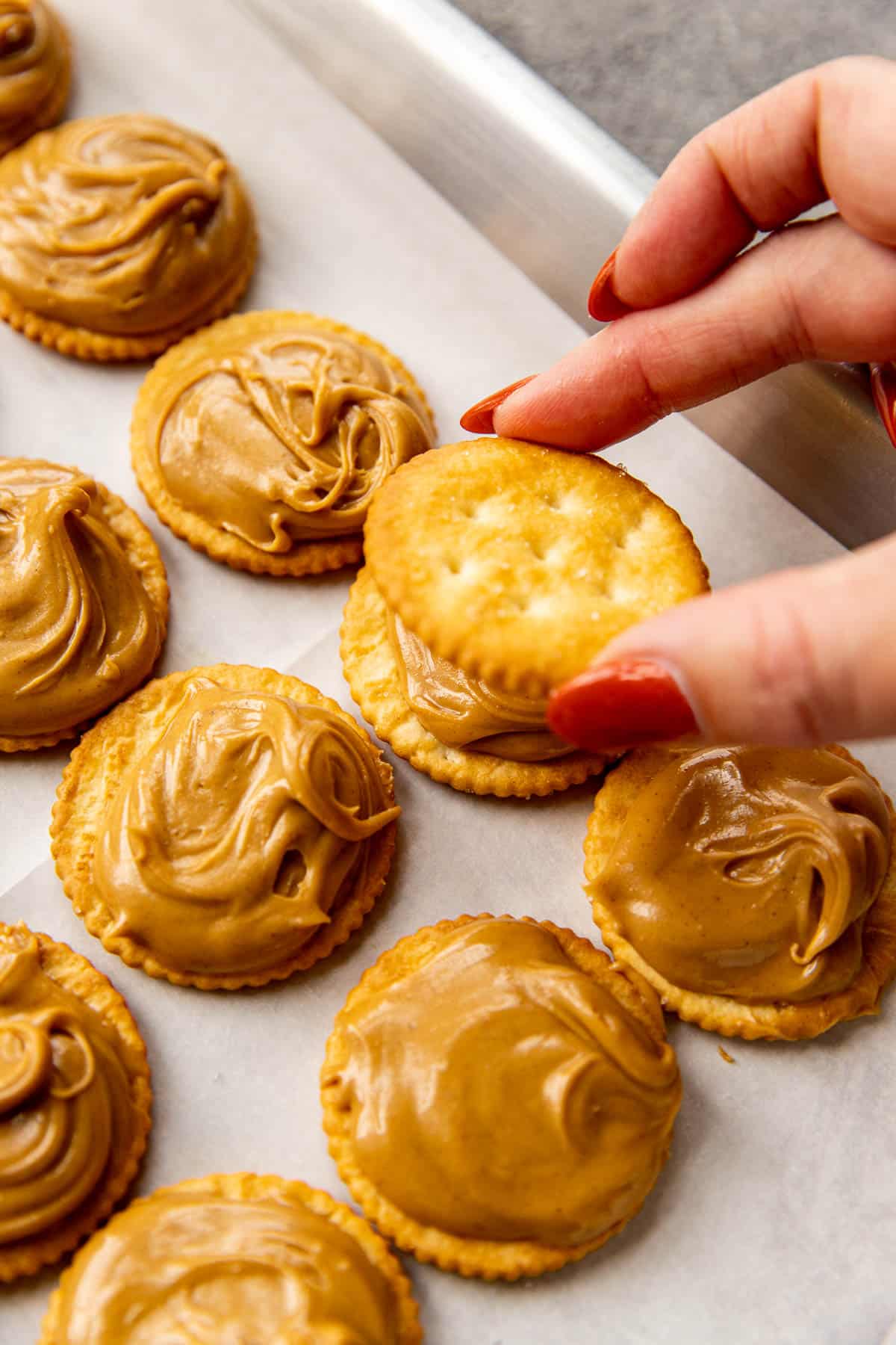 a hand placing a ritz cracker on top of peanut butter. 
