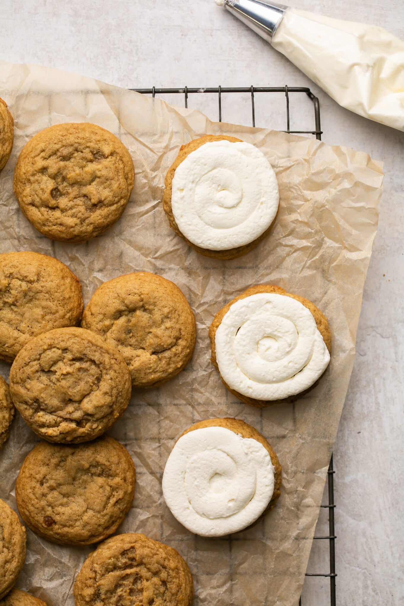 cookies being frosted with mascarpone frosting on parchment paper. 