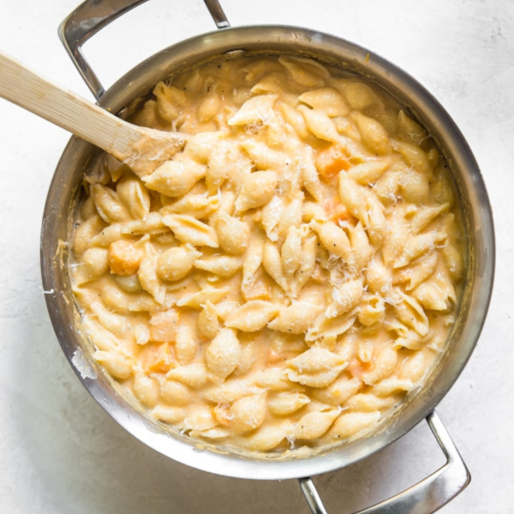 large pot full of shell noodles and light yellow cream sauce, and spoon