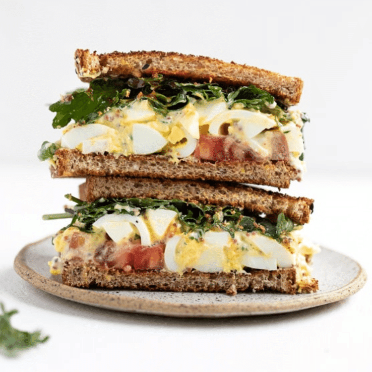halves of brown bread with egg salad, lettuce and tomatoes on a plate