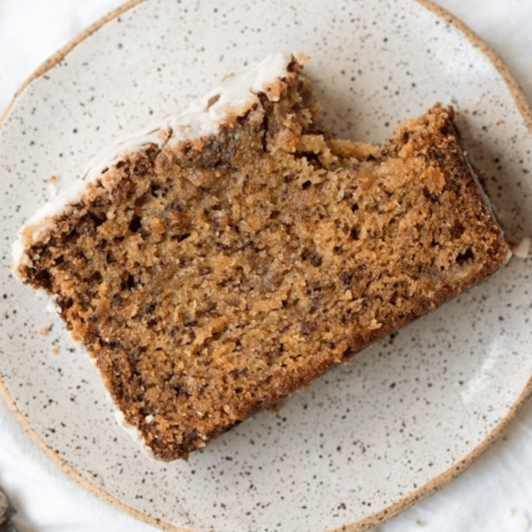 speckled white plate with a slice of banana bread with a white glaze